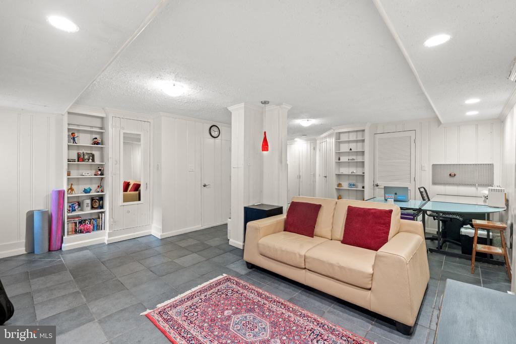 Finished basement recreation room with built-in shelves, gray tile floors, and a beige sofa.