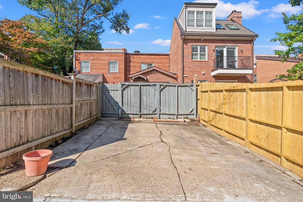 Red-brick home beyond a paved driveway enclosed by wooden fences.