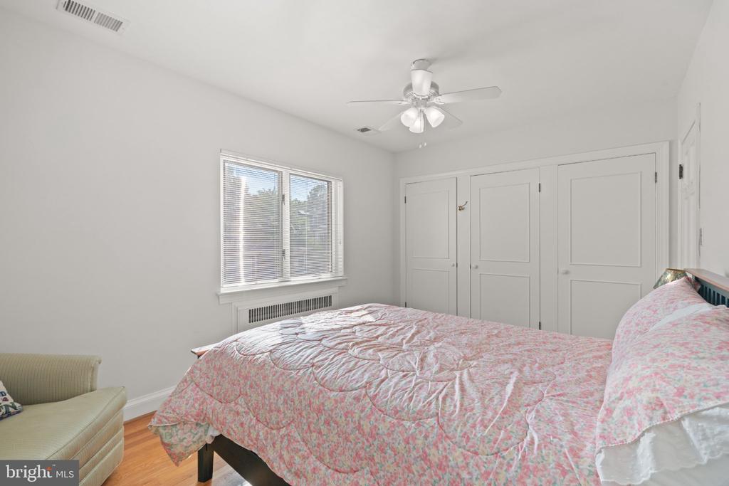 Bedroom with a pink floral quilt, built-in closets, and a window with blinds.