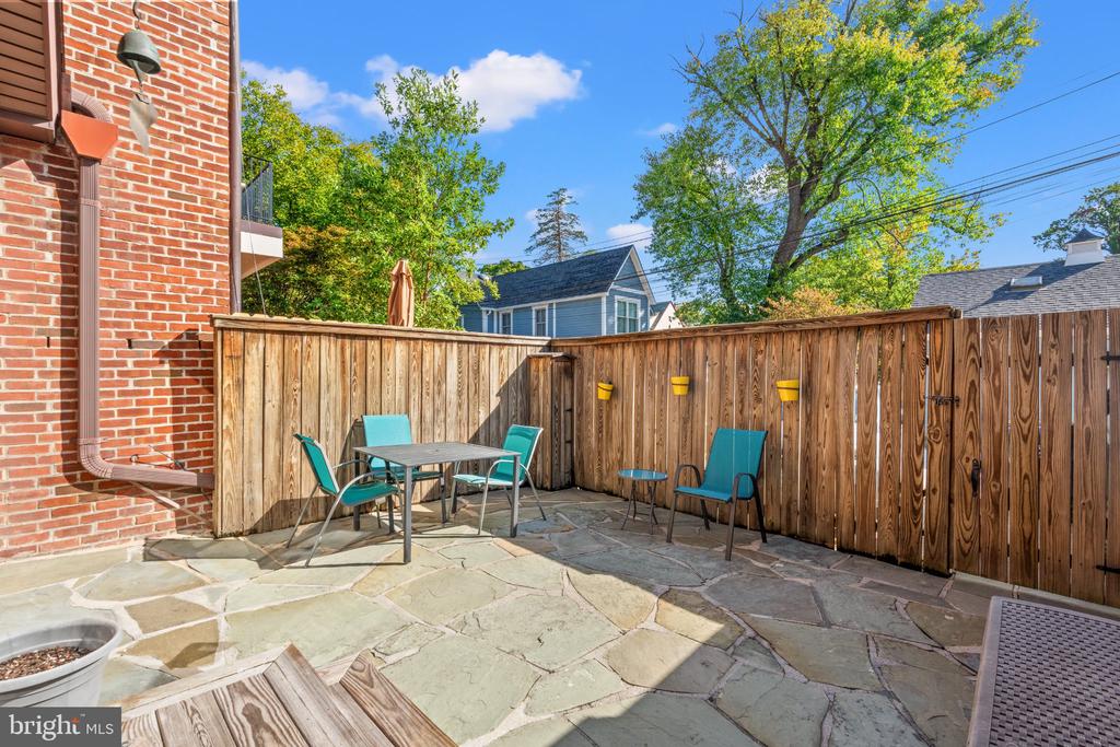 Flagstone patio with turquoise outdoor seating, a wooden privacy fence, and a red brick house.
