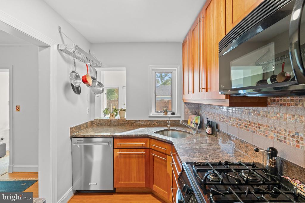 Kitchen with warm wood cabinets, granite counters, mosaic backsplash, and a stainless steel gas range.