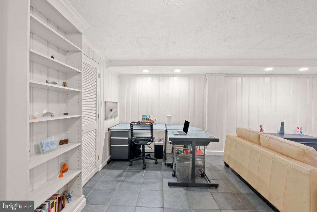 Home office with built-in white shelves, a desk, and a tan sectional sofa.