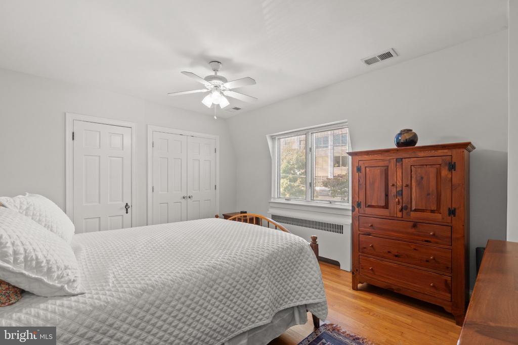 Bedroom with a white quilted bed, wooden armoire, and hardwood floors.