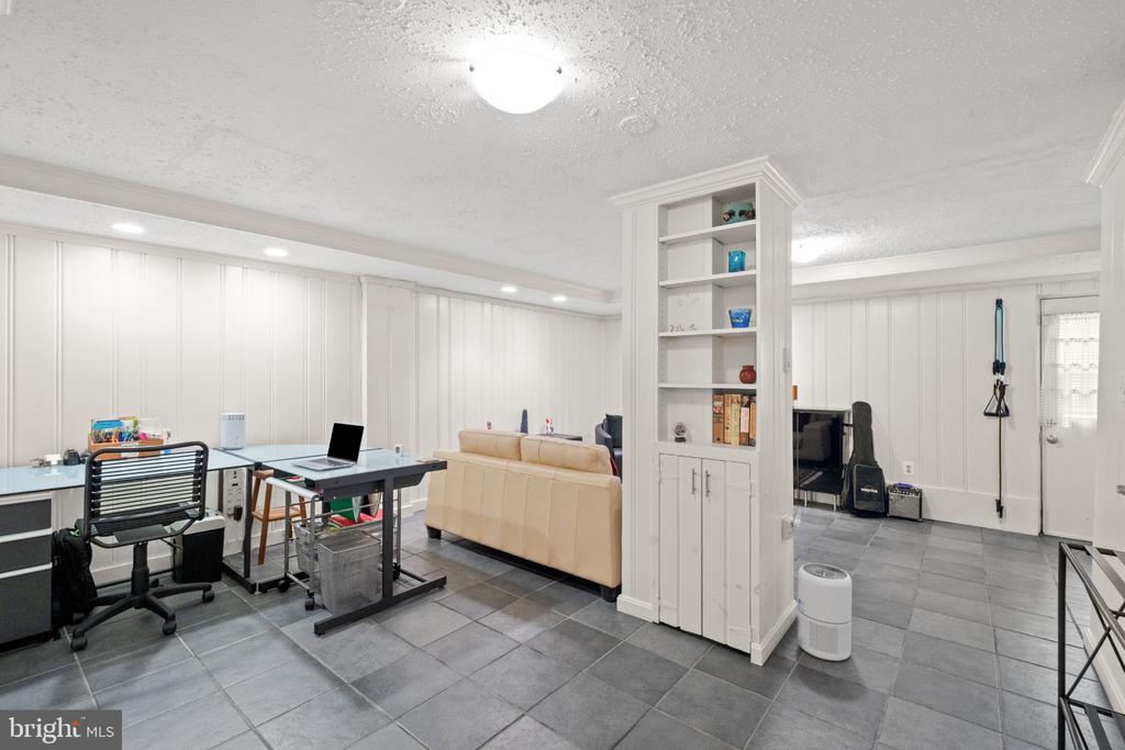 Finished basement with a desk, tan sofa, and built-in shelving.