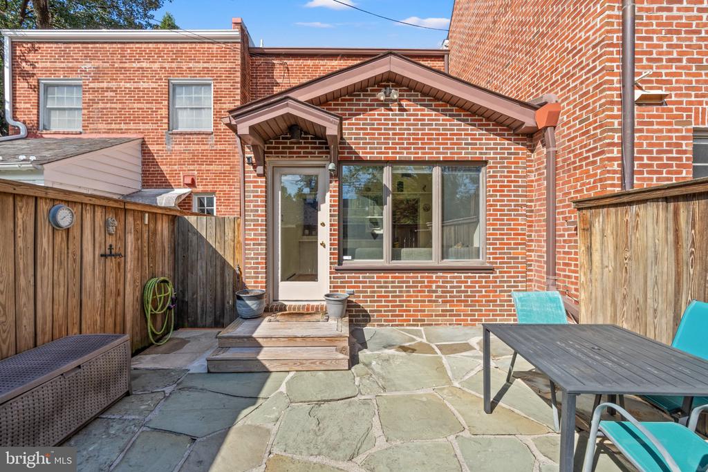 Brick home's fenced stone patio with wooden steps, a dining table, and turquoise chairs.