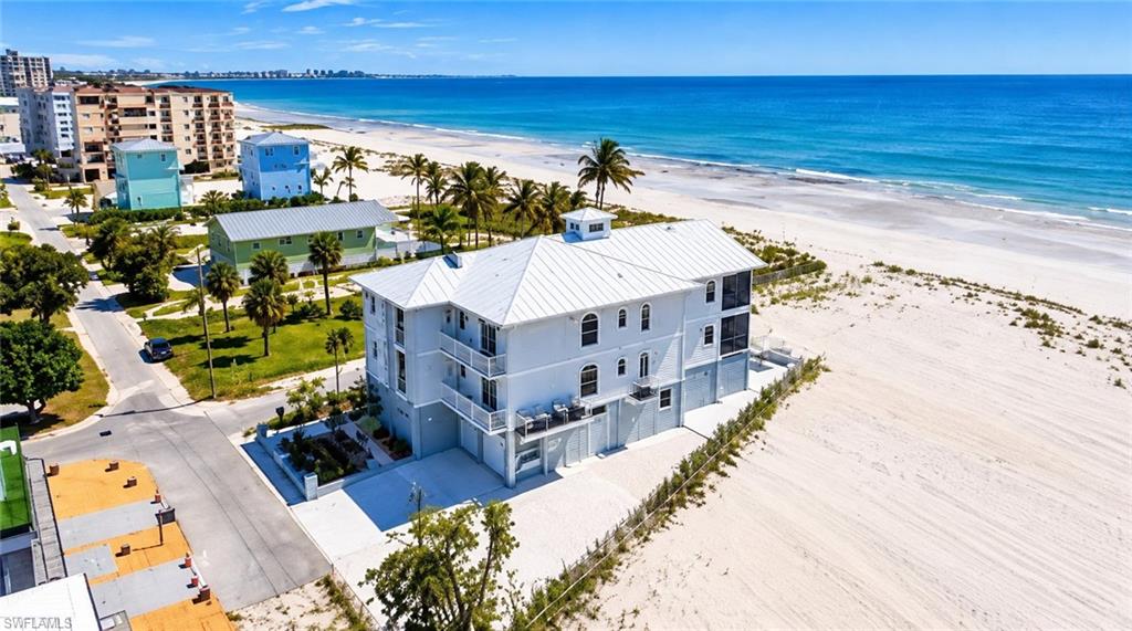 White multi-story beachfront building with balconies and a light metal roof beside a sandy beach.
