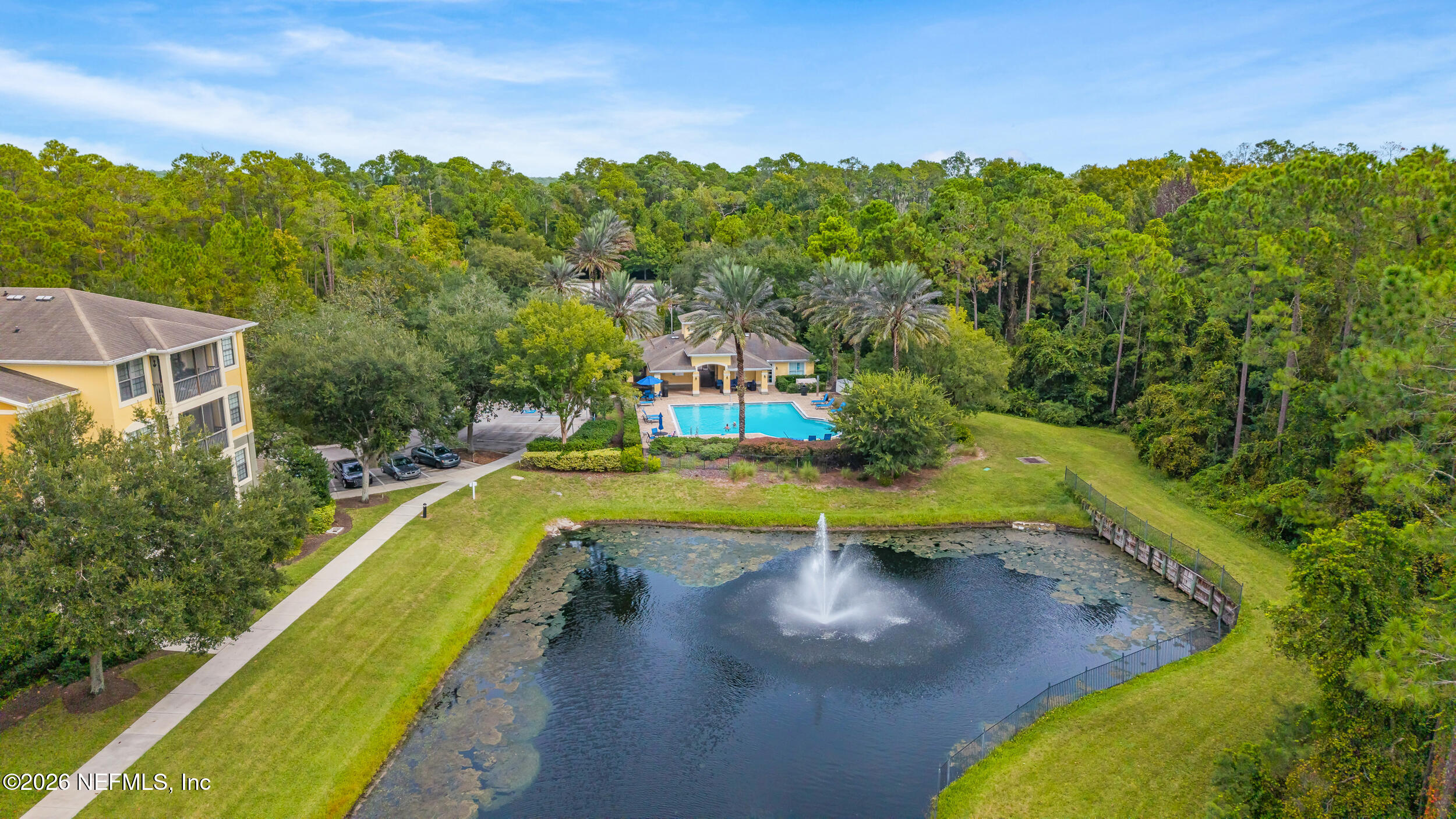 Aerial view of community pool and fountain pond surrounded by trees and walking paths.