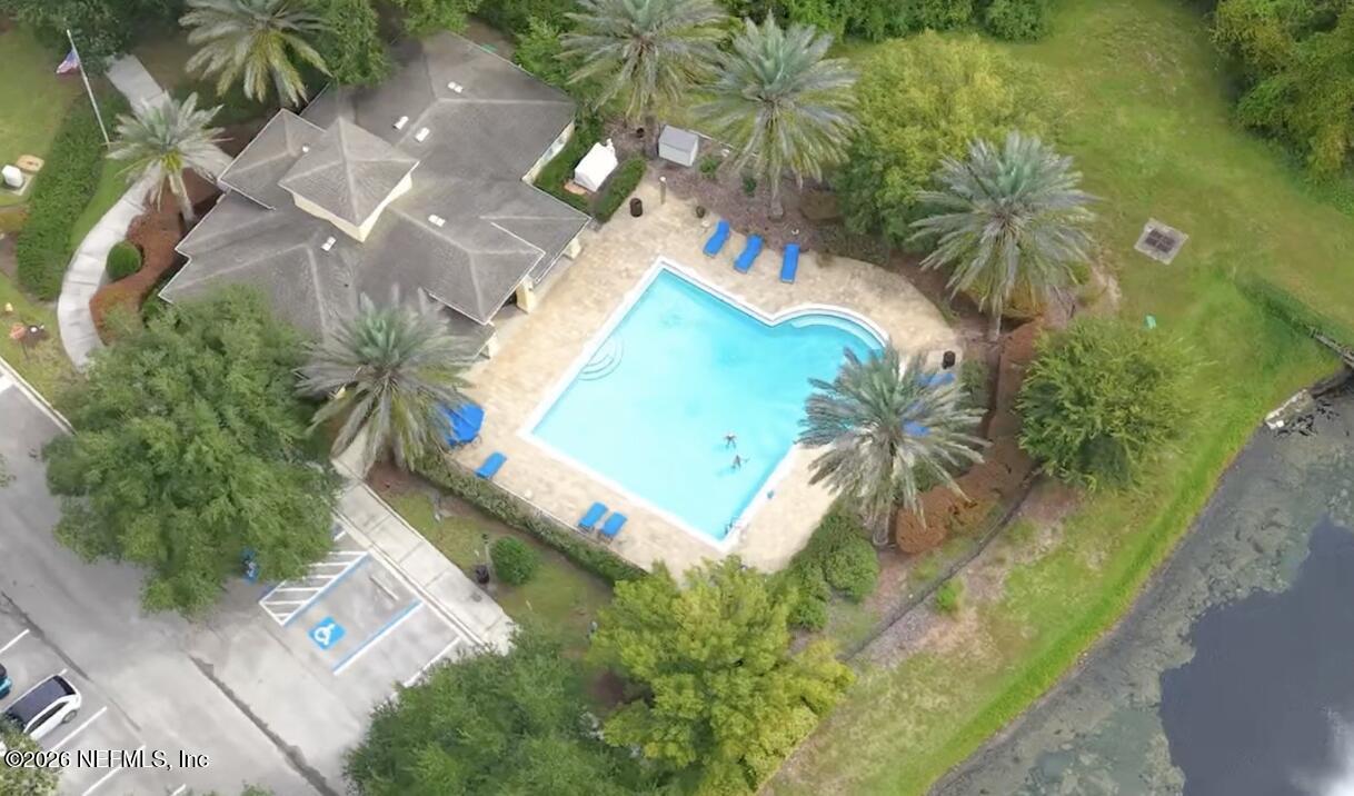 Aerial view of a home with a pool, palm trees, and a waterfront edge.