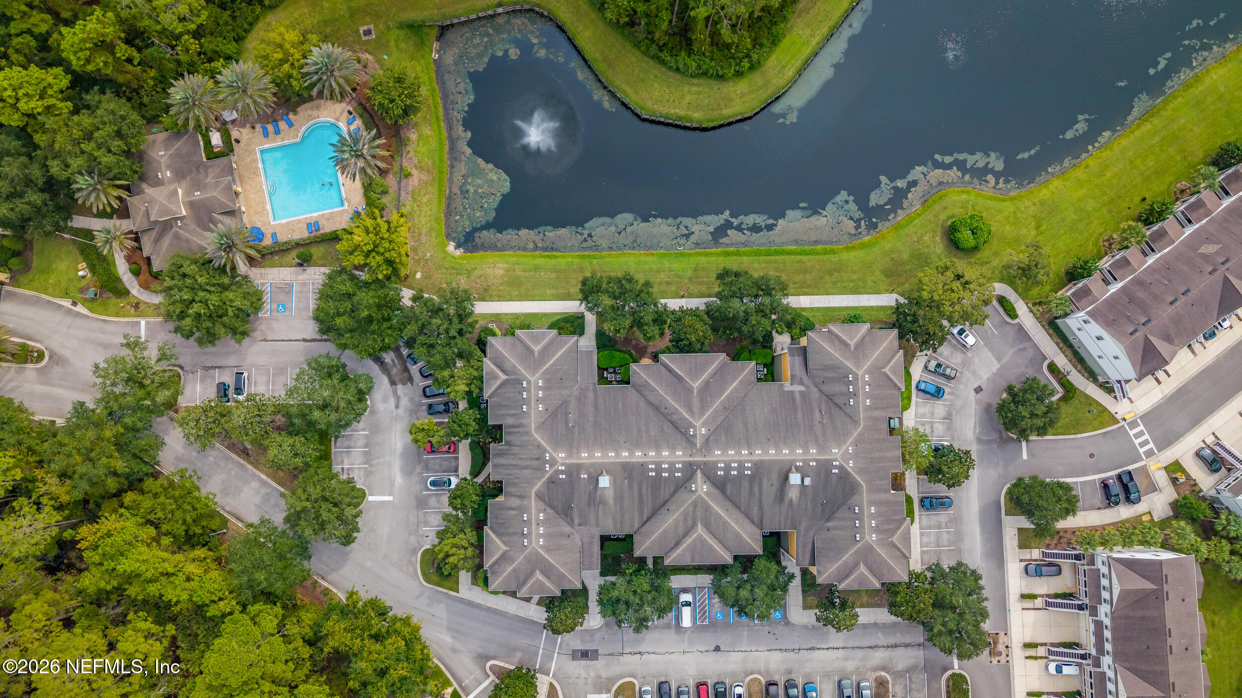 Aerial view of a residential community with a pool and fountain pond beside its central building.
