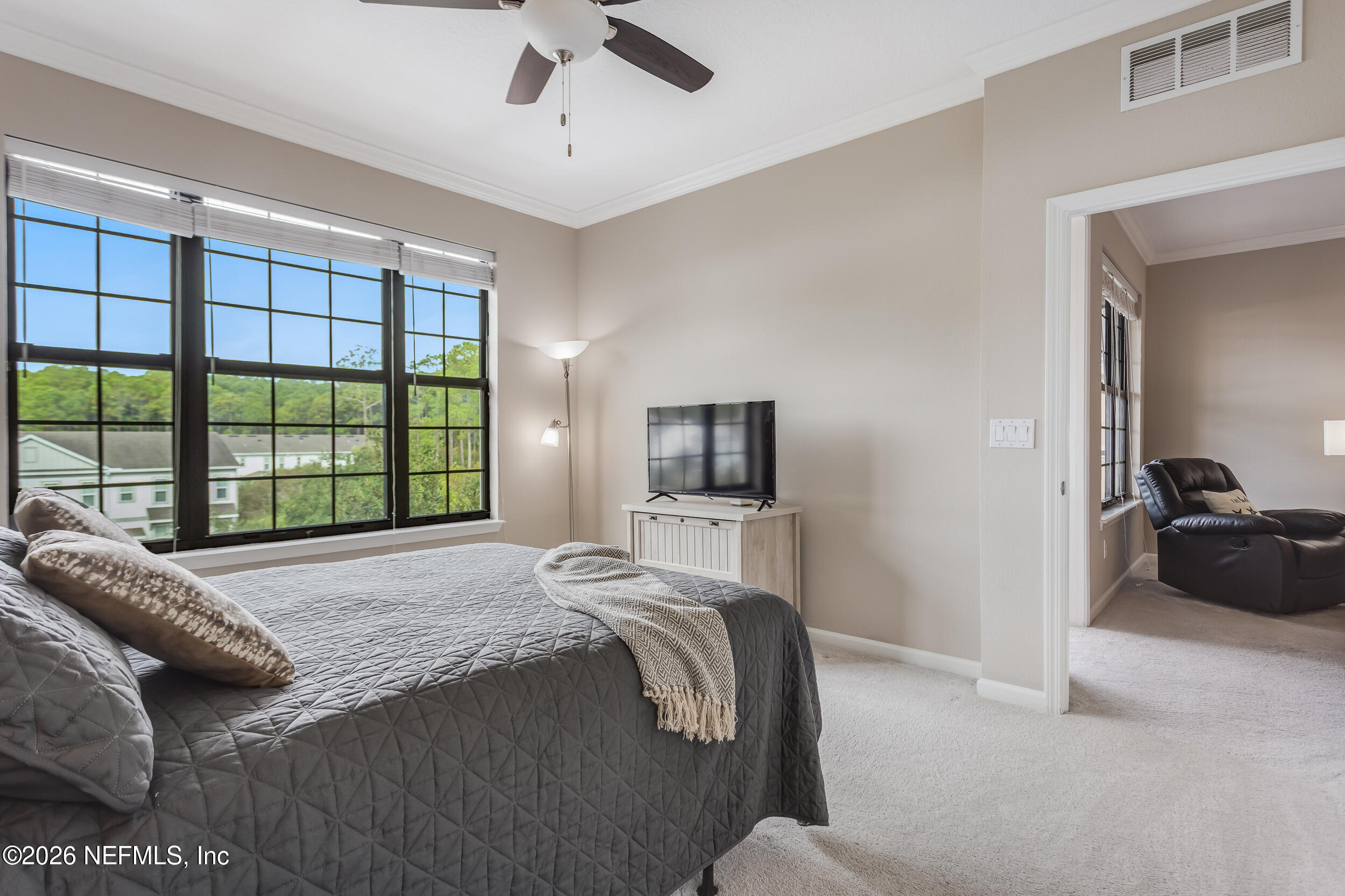 Bedroom with a charcoal quilted bed beside large grid windows; an adjoining sitting area has a leather recliner.