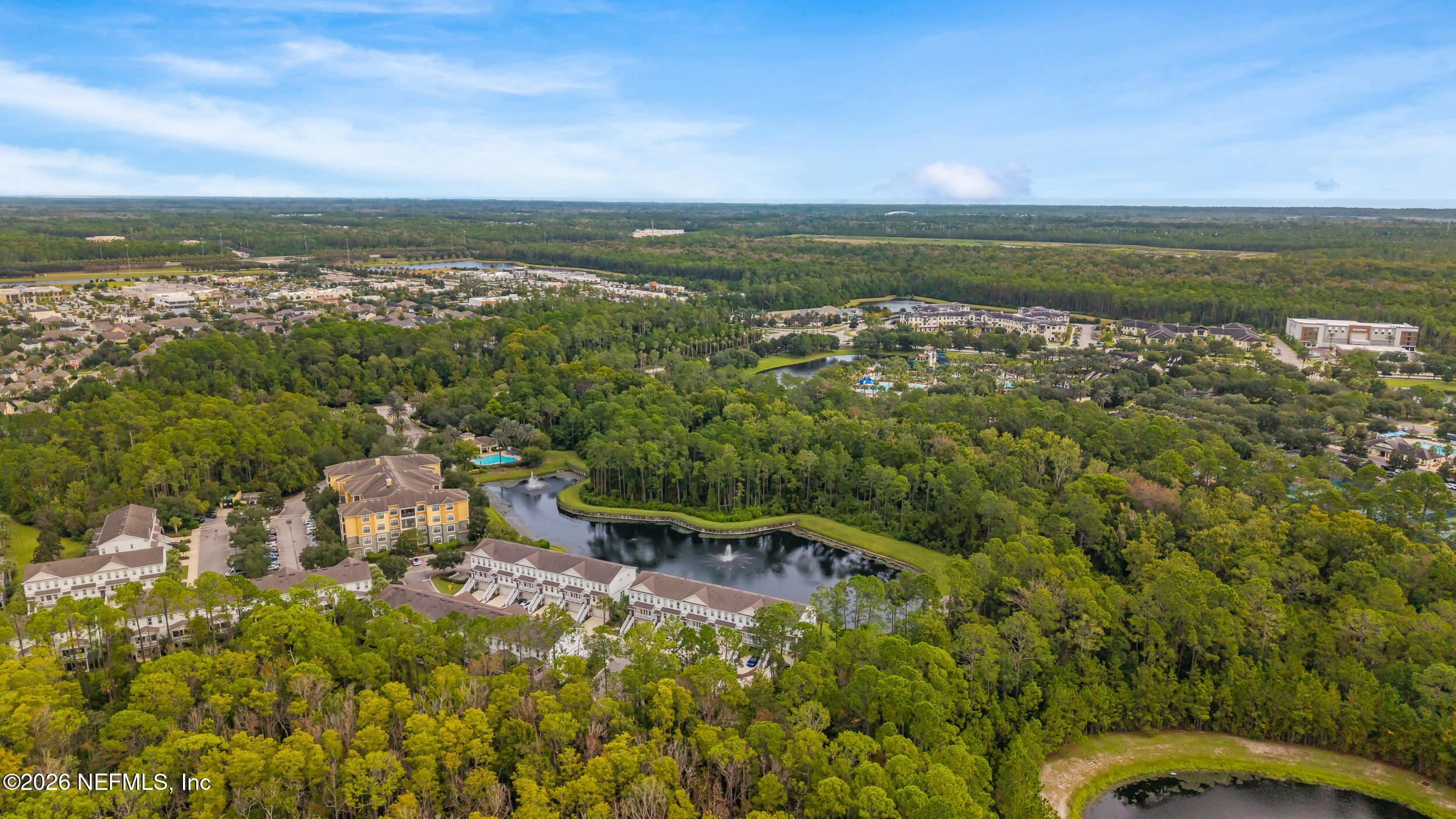 Aerial view of a wooded residential community with ponds, fountains, and clustered buildings.