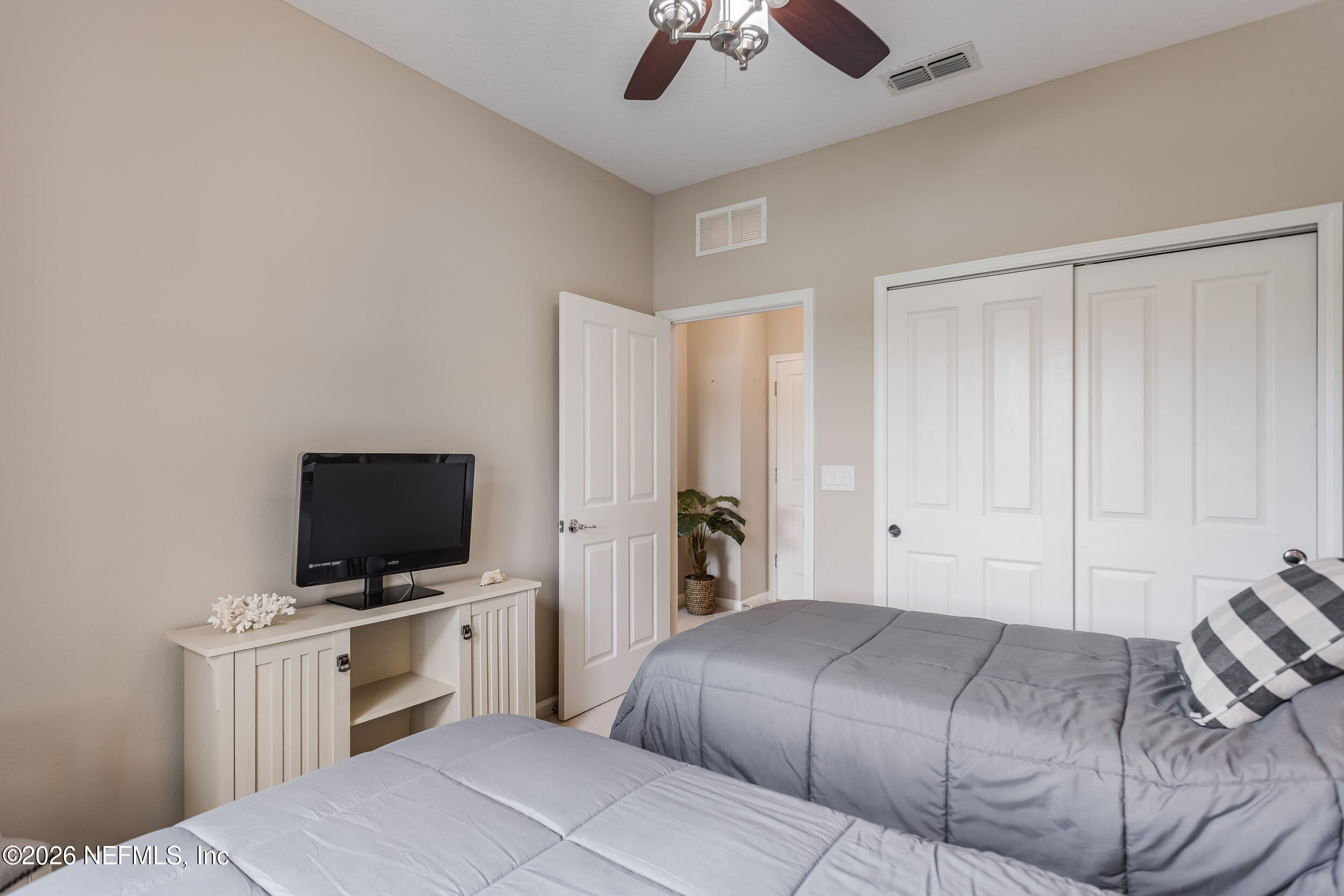 Bedroom with two gray-covered beds, white closet doors, and a television on a cabinet.