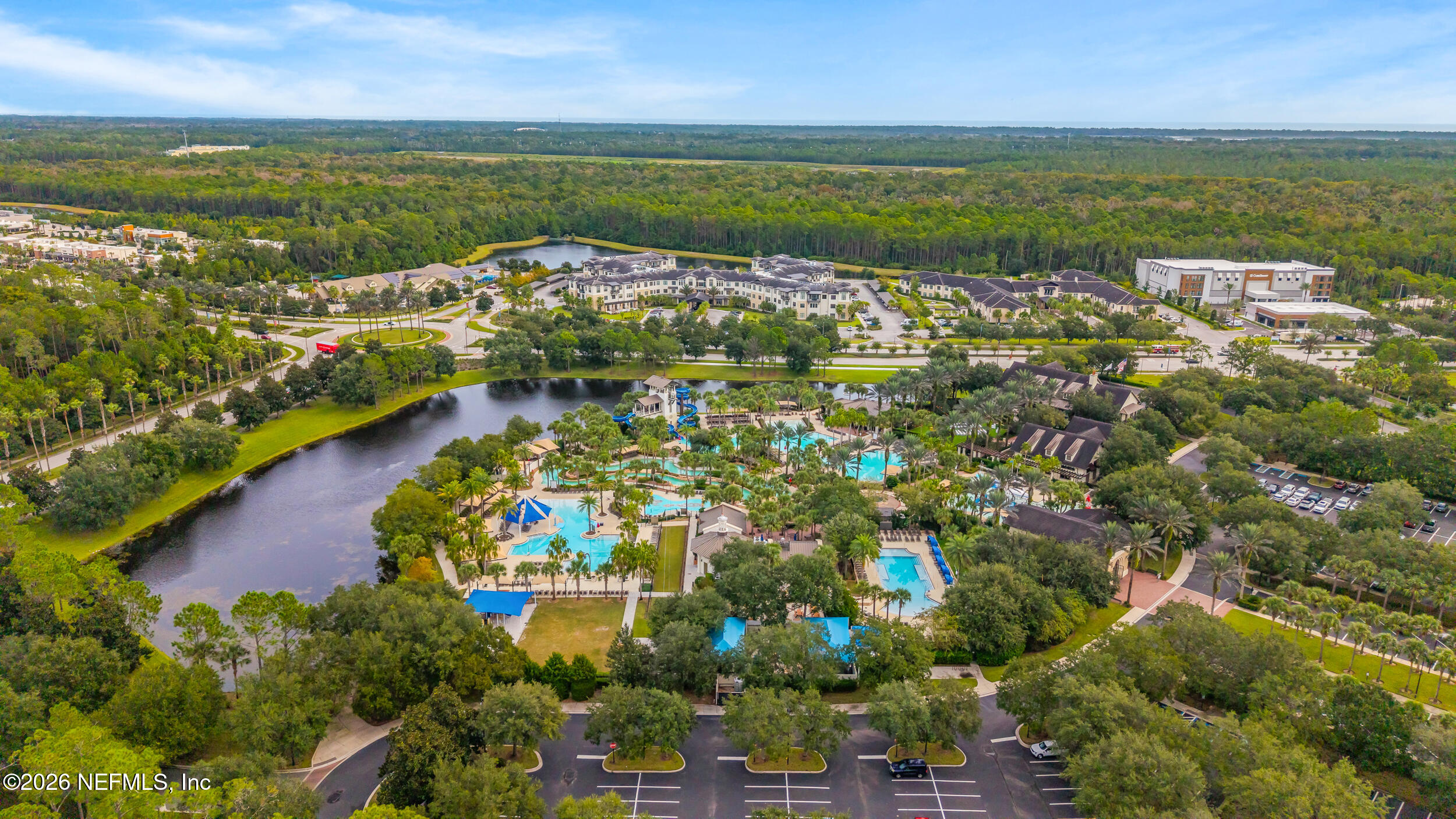 Aerial view of a residential community with palm-lined pools, waterslides, and a pond.