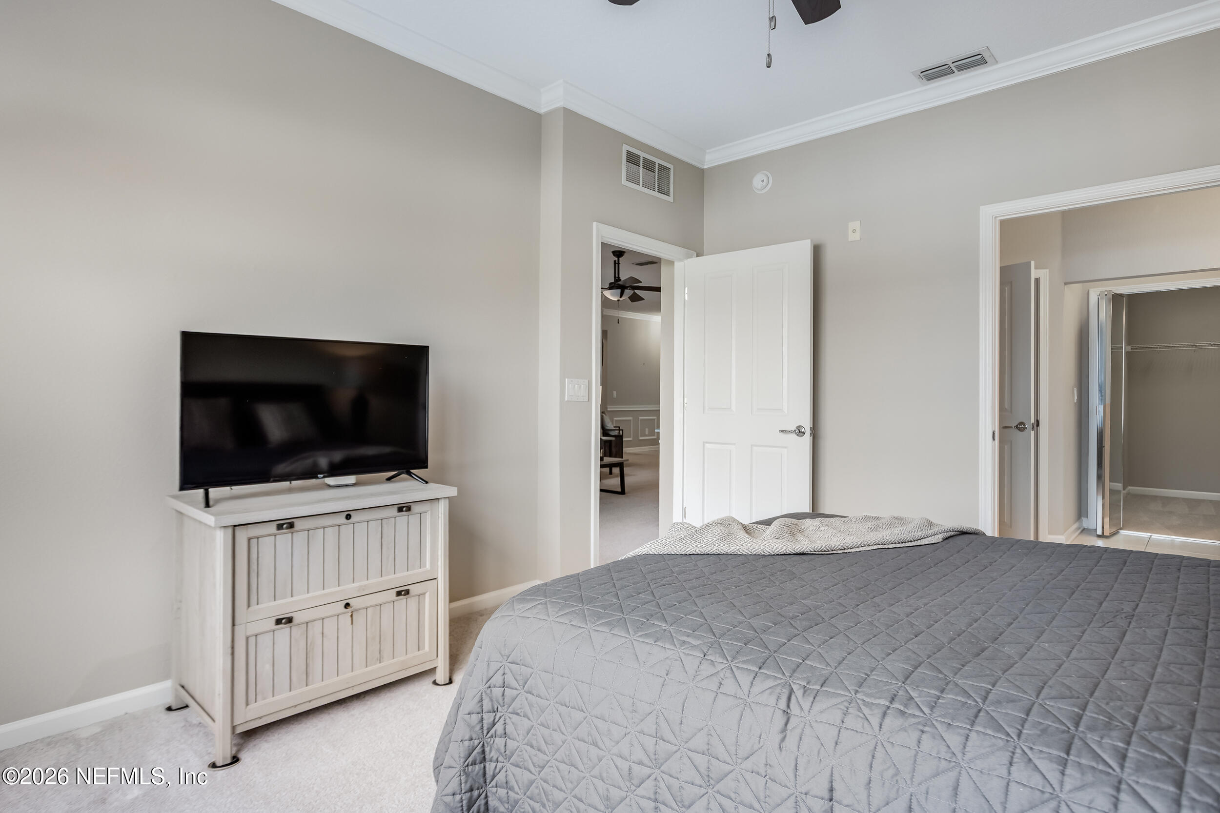 Bedroom with a gray quilted bed, television on a white dresser, and open walk-in closet.
