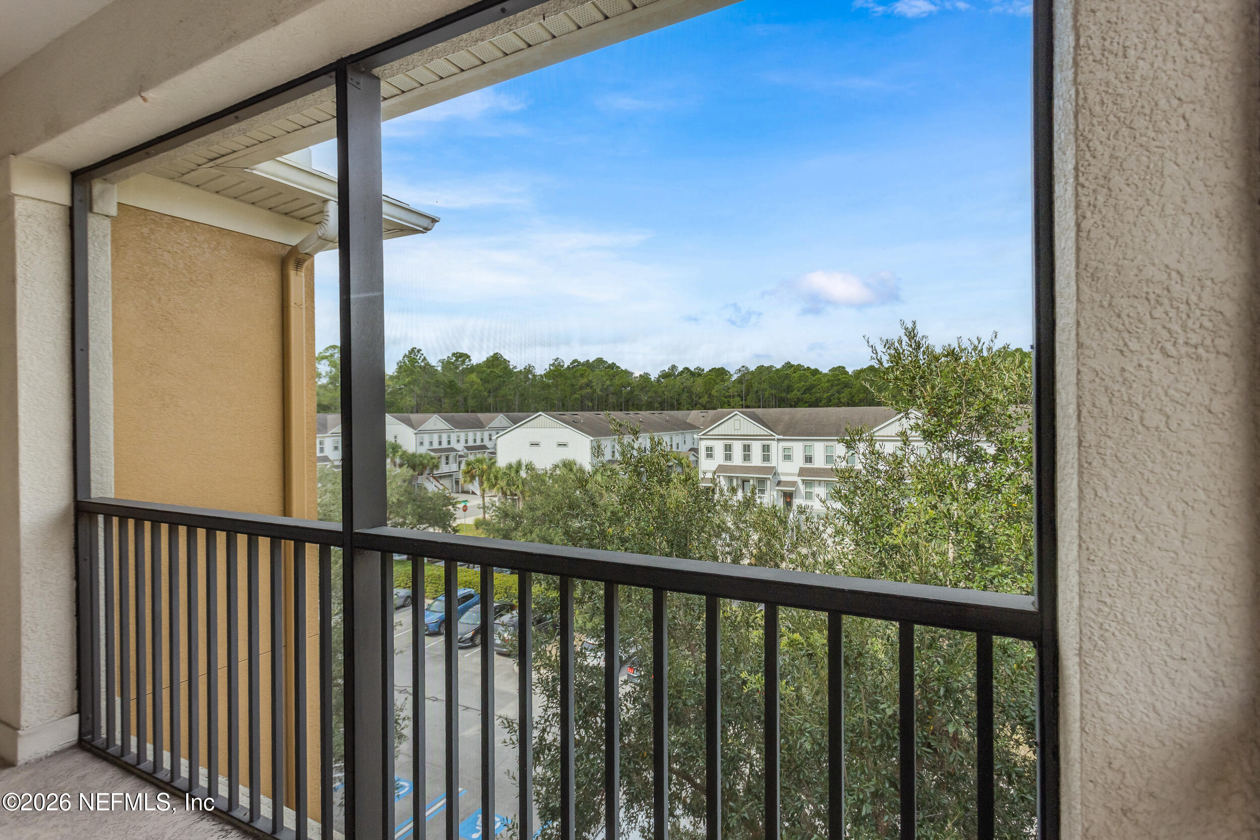 Screened balcony overlooking leafy trees and neighboring townhomes.