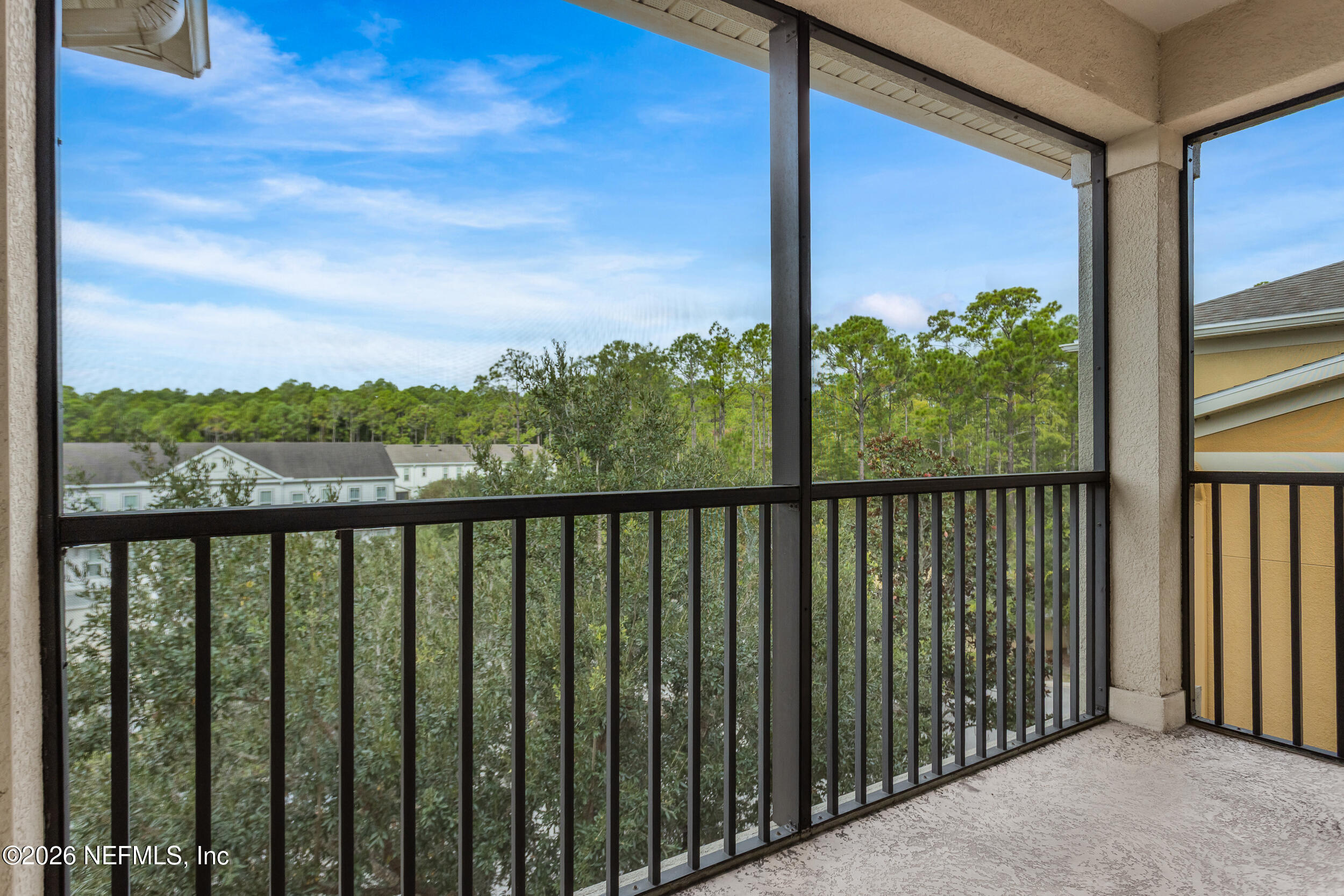 Screened balcony overlooking trees and neighboring homes, with black railings and a light textured floor.