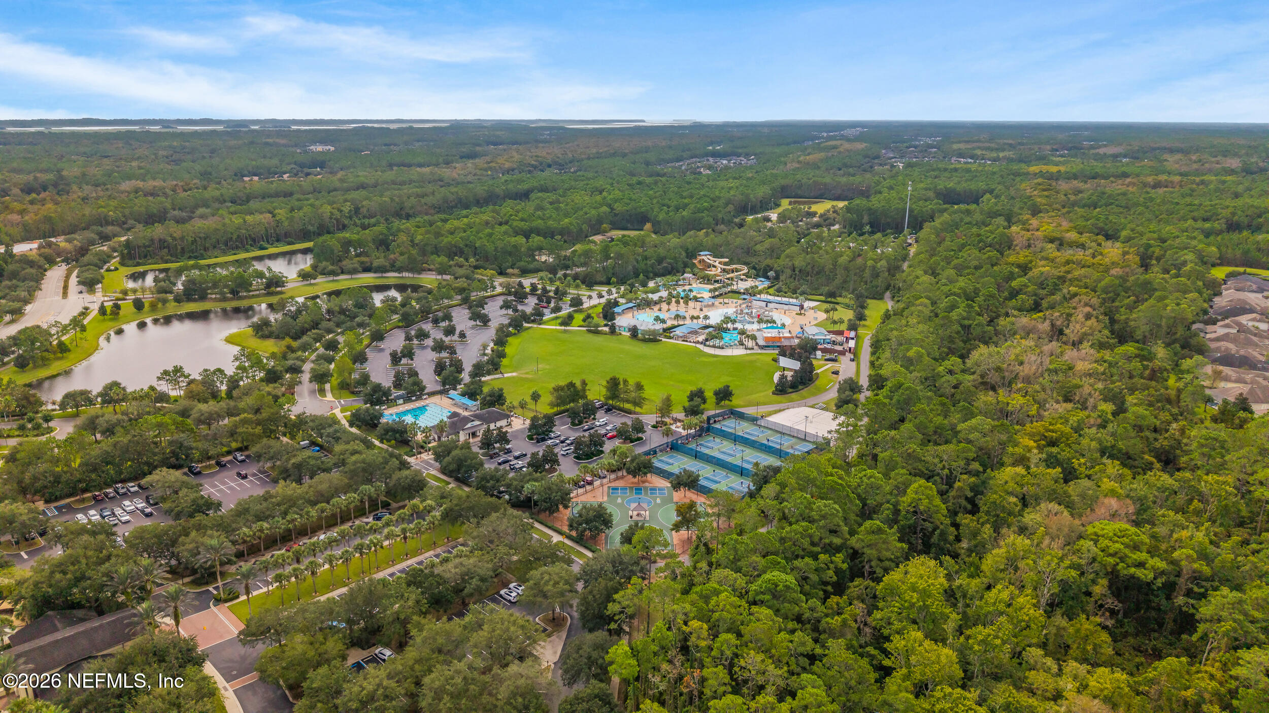 Aerial view of community pools, water slides, courts, ponds, and a broad green lawn amid trees.
