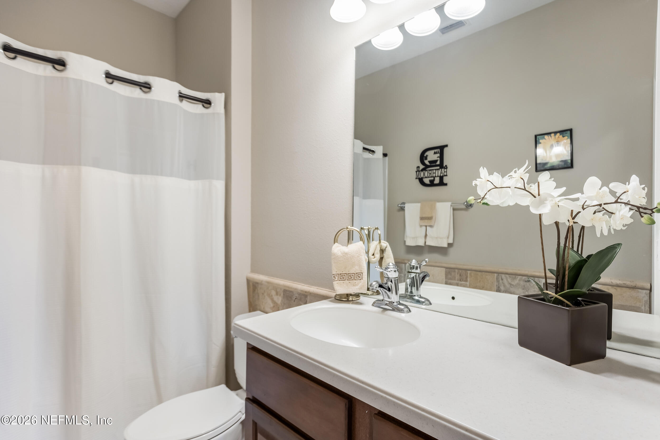 Bathroom vanity with a white sink, dark wood cabinets, large mirror, and white orchid.