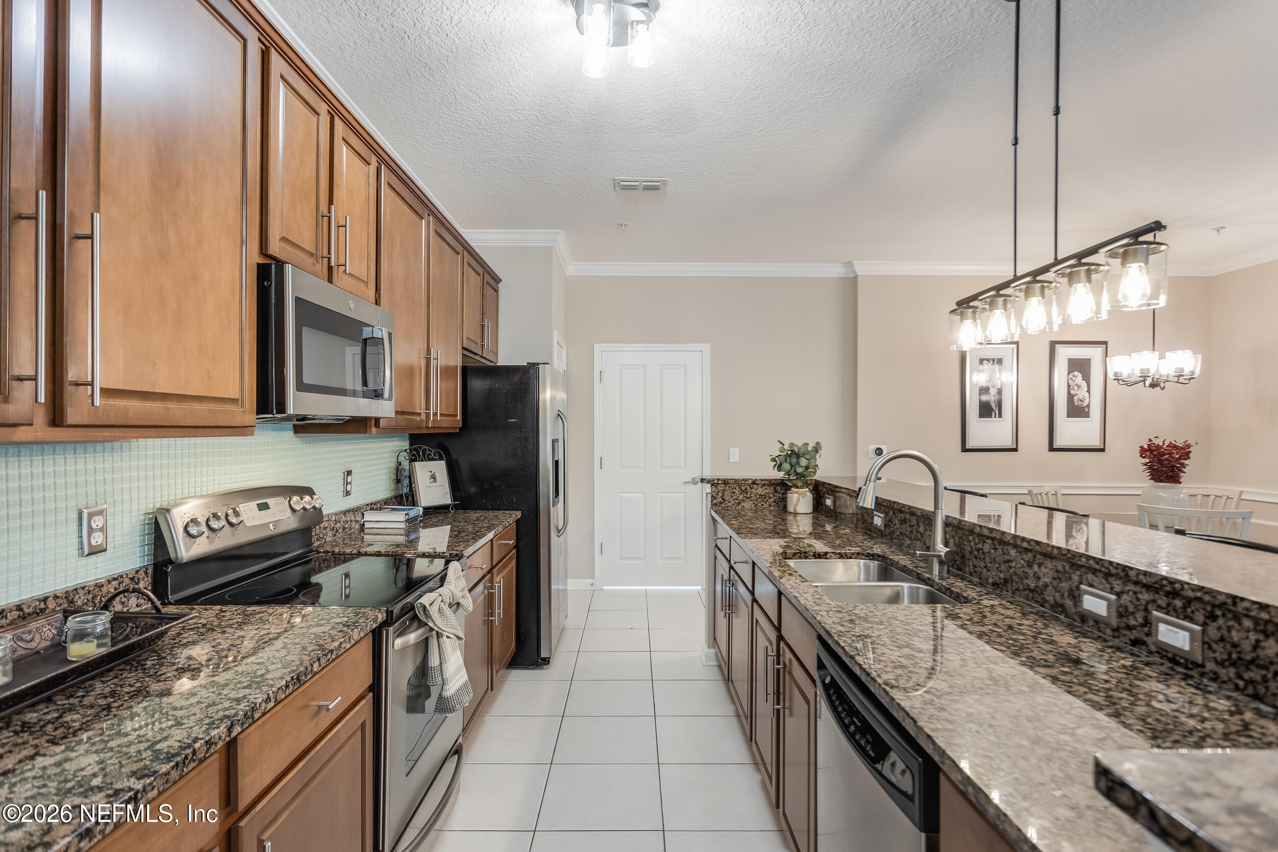 Kitchen with warm wood cabinets, granite counters, stainless steel appliances, and a long island with a double sink.