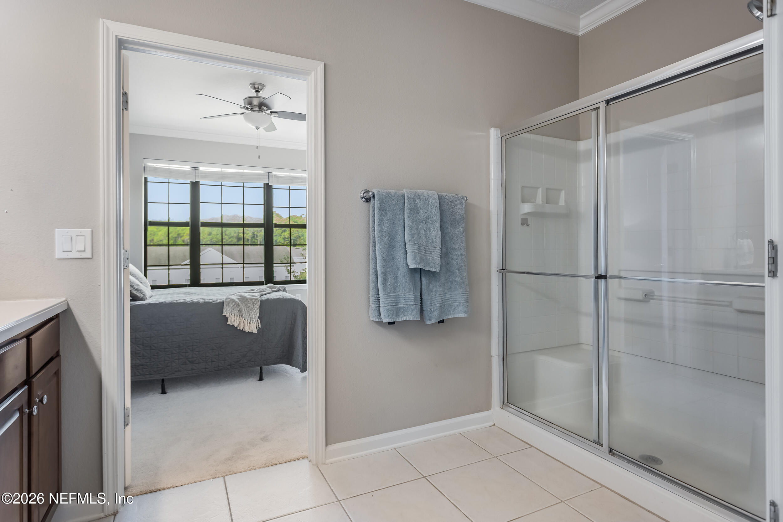 Bathroom with a glass-enclosed shower and blue towels, looking through to a bedroom with wide windows.