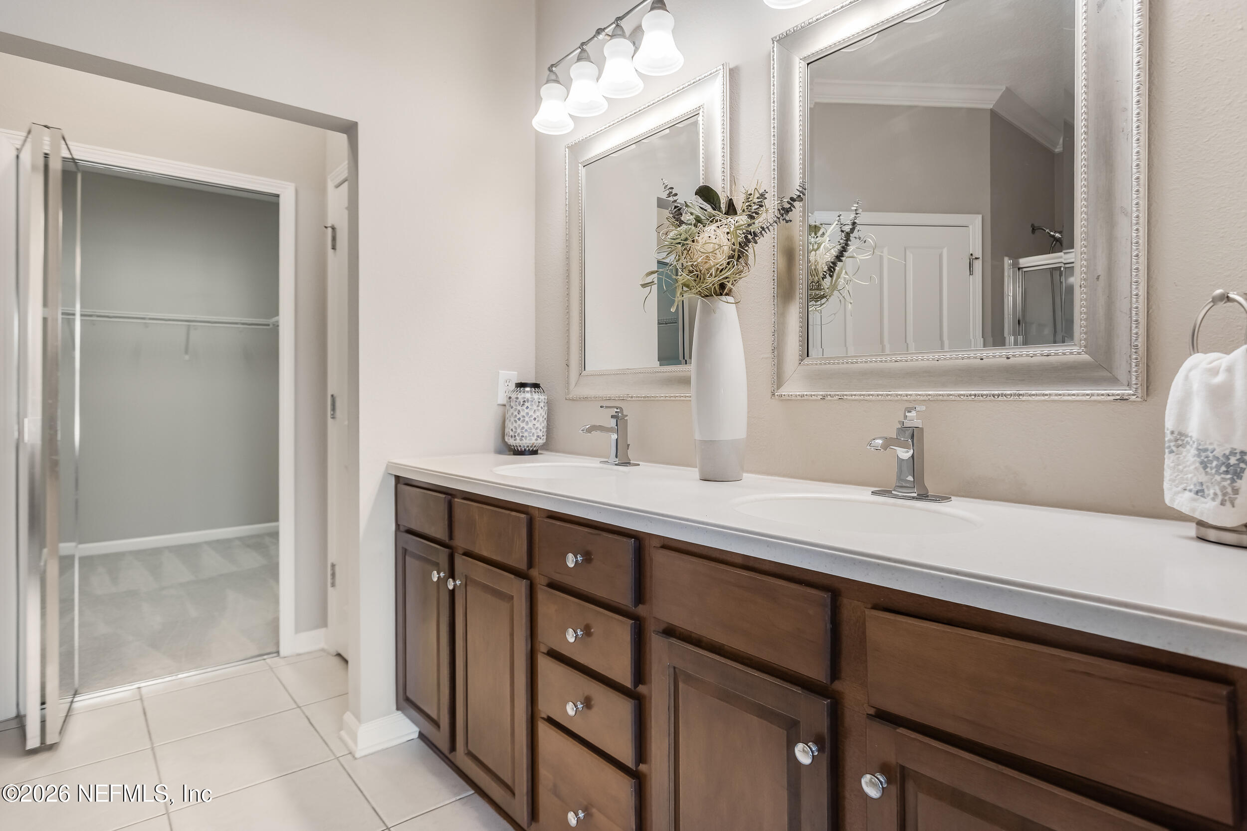 Bathroom with a dark wood double vanity, two sinks, and framed mirrors beside an open closet.