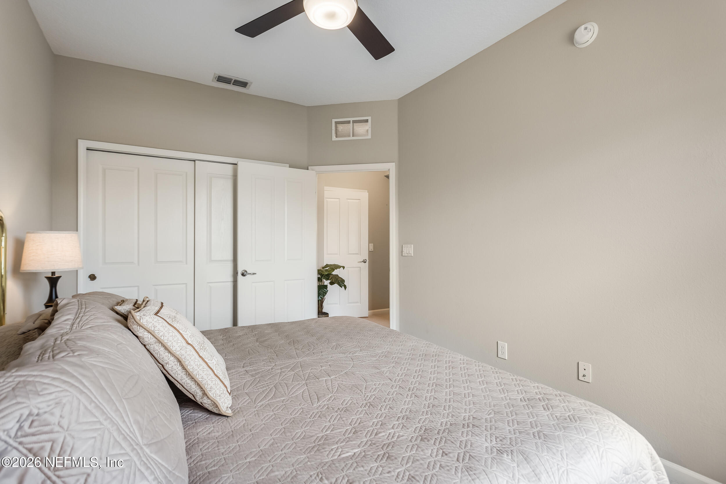 Furnished bedroom with a quilted gray bed, white paneled closet doors, and an open doorway.