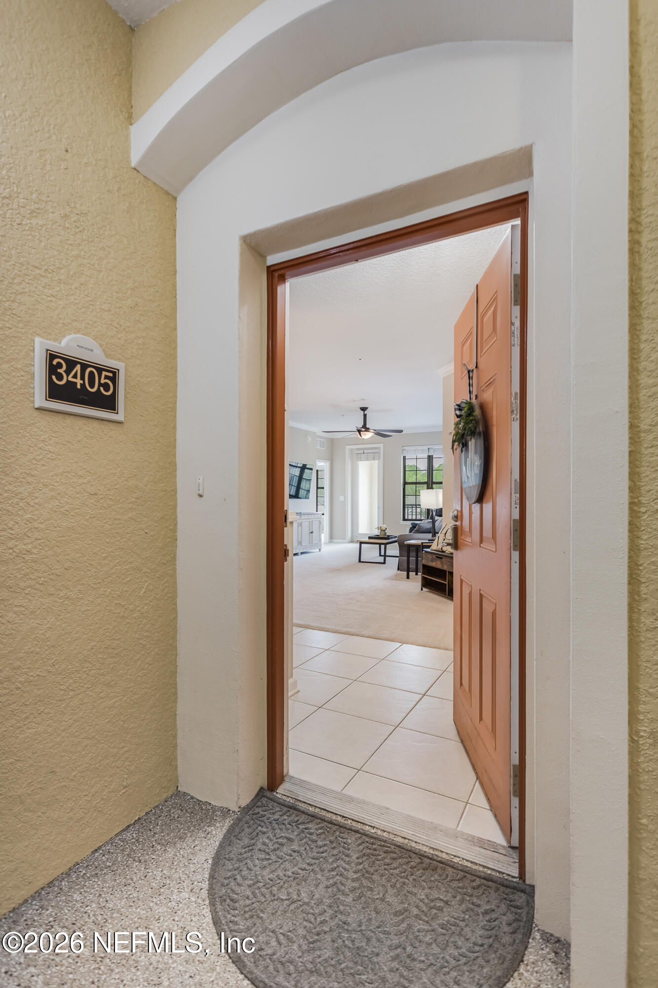Open wood front door reveals a bright living room with tiled entry and a 3405 unit plaque.