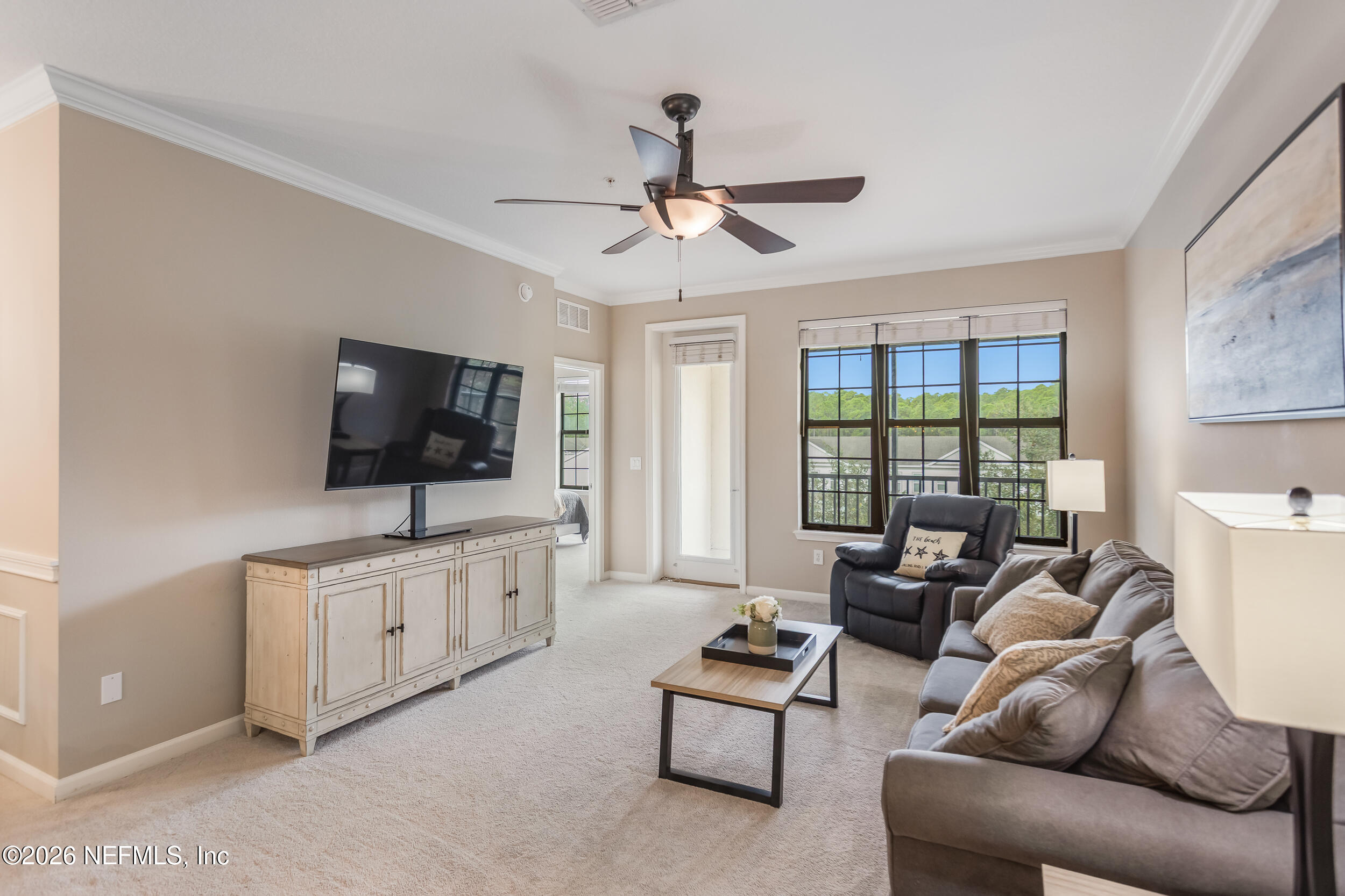 Furnished living room with a sectional sofa, television, and windows overlooking trees.