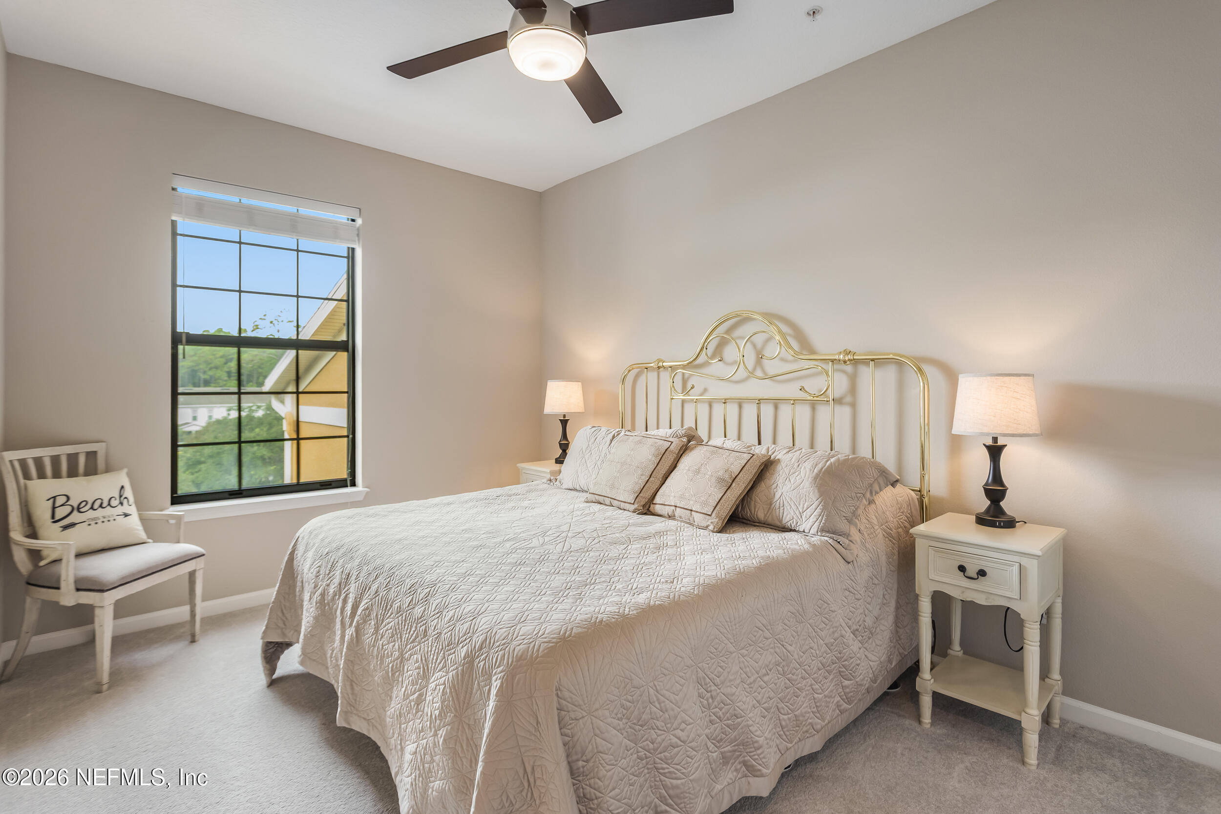 Bedroom with a brass bed, pale quilt, bedside lamps, and a window overlooking greenery.