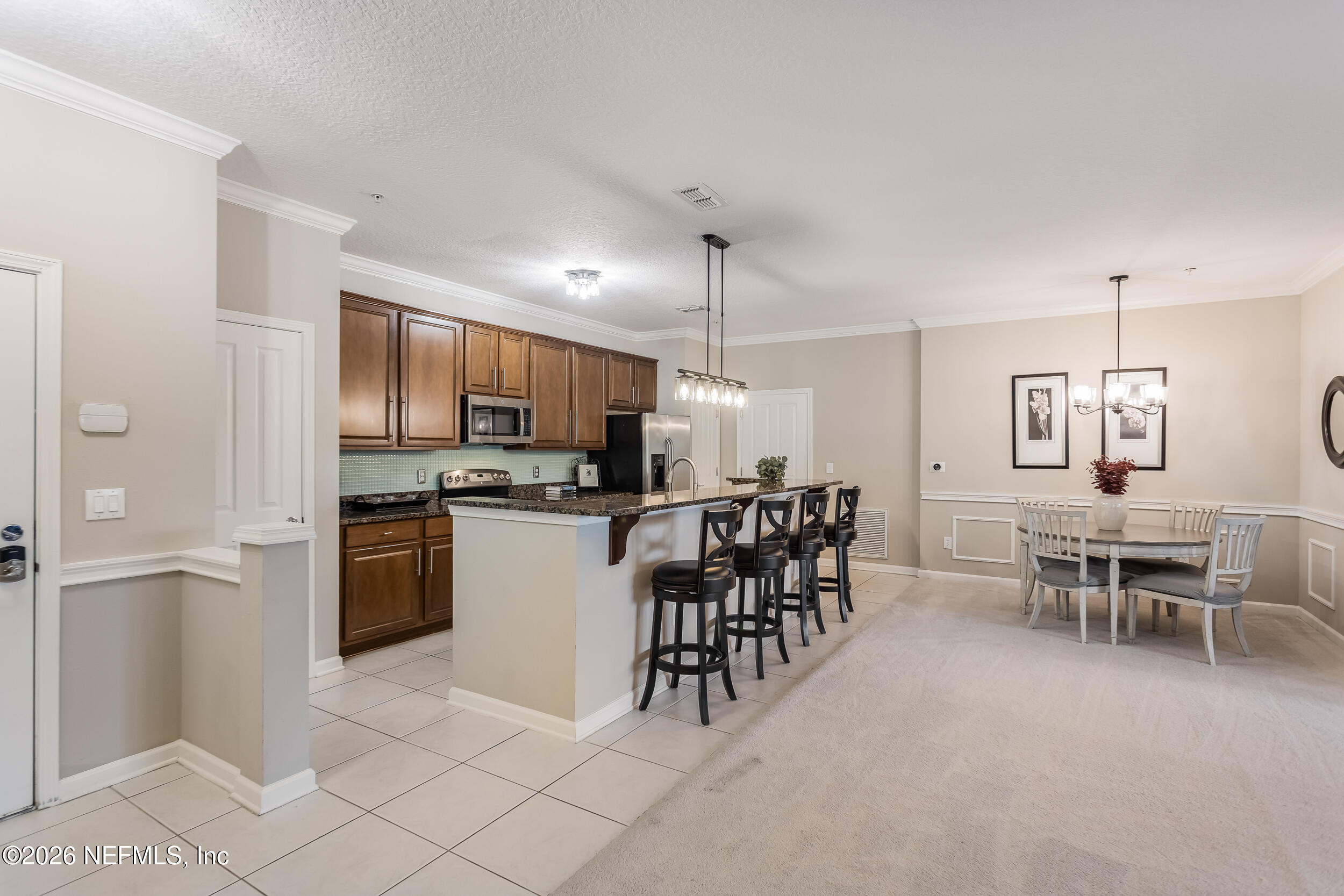 Open-plan kitchen and dining area with granite island, bar stools, and dark wood cabinets.