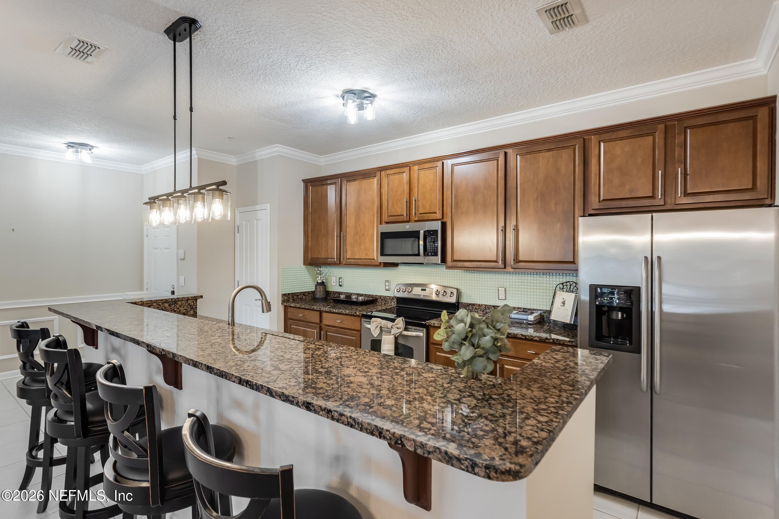 Kitchen with dark wood cabinets, stainless steel appliances, and a granite island with bar stools.