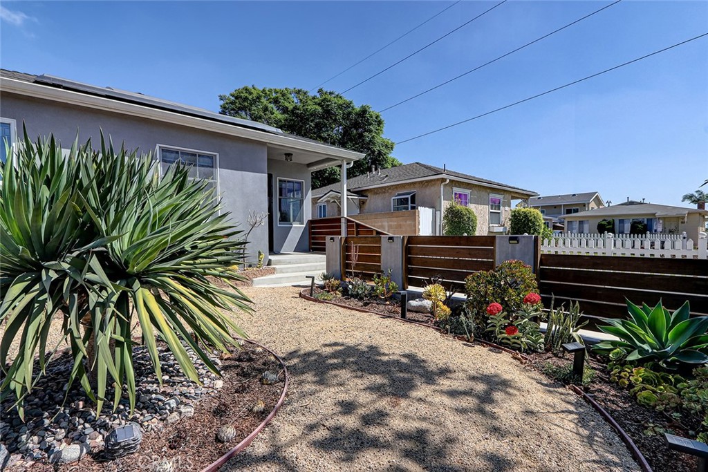 Gray home beside a landscaped gravel yard with large spiky plants and a dark slat fence.