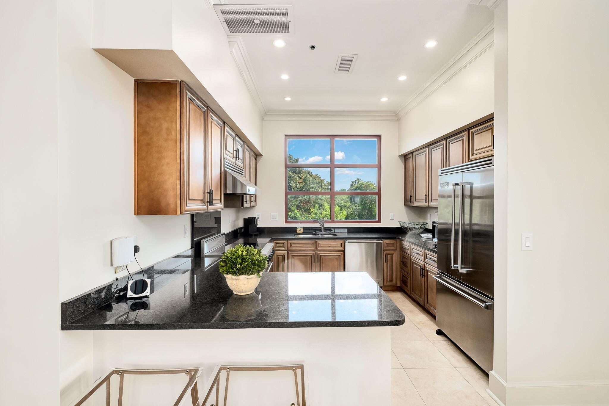 Kitchen with wood cabinets, black granite counters, stainless appliances, and a large window overlooking trees.