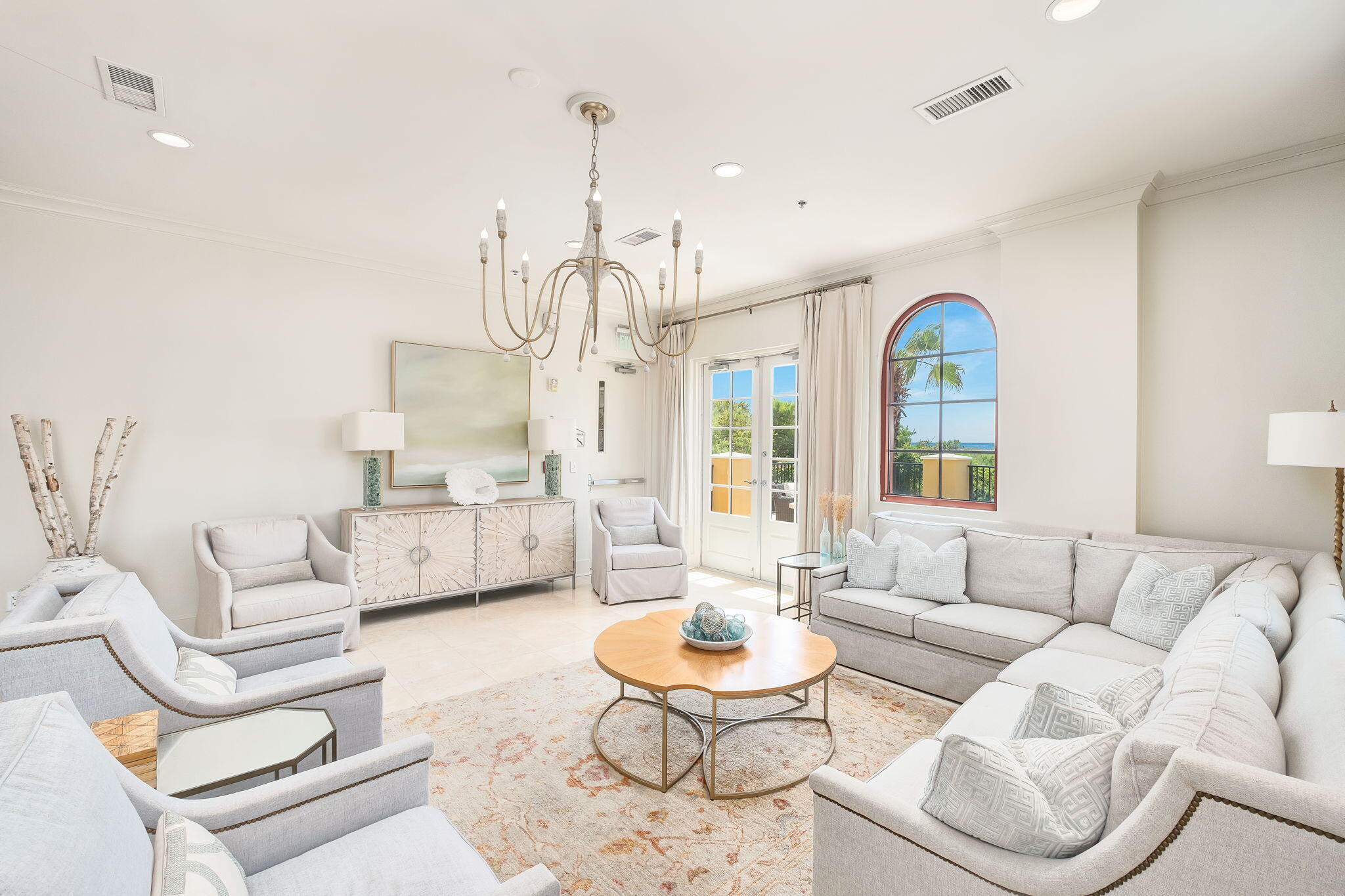 Staged living room with pale seating, a chandelier, and an arched window overlooking the water.