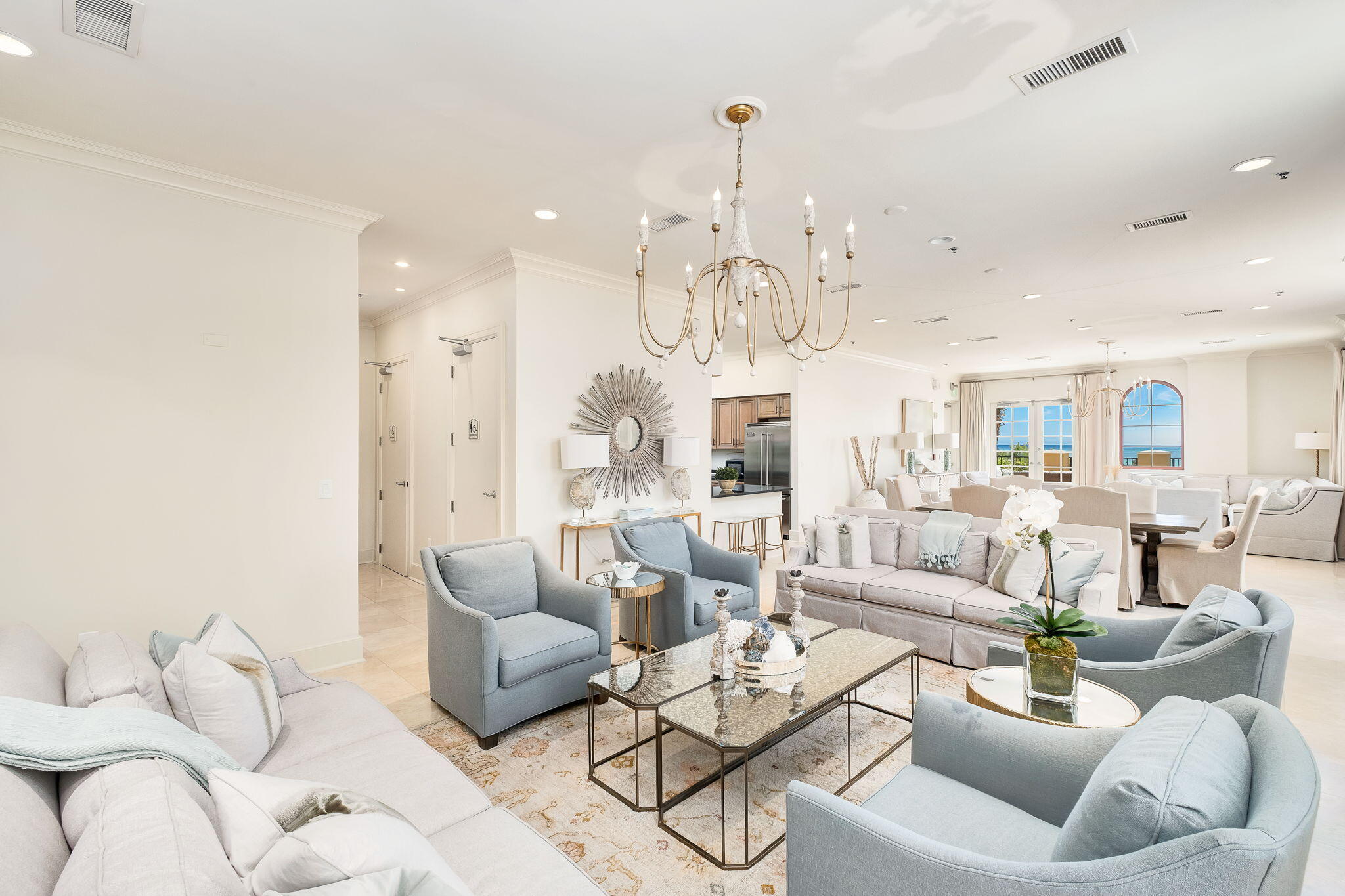 Open-plan condo living room with pale blue seating, a chandelier, and water visible through the windows.