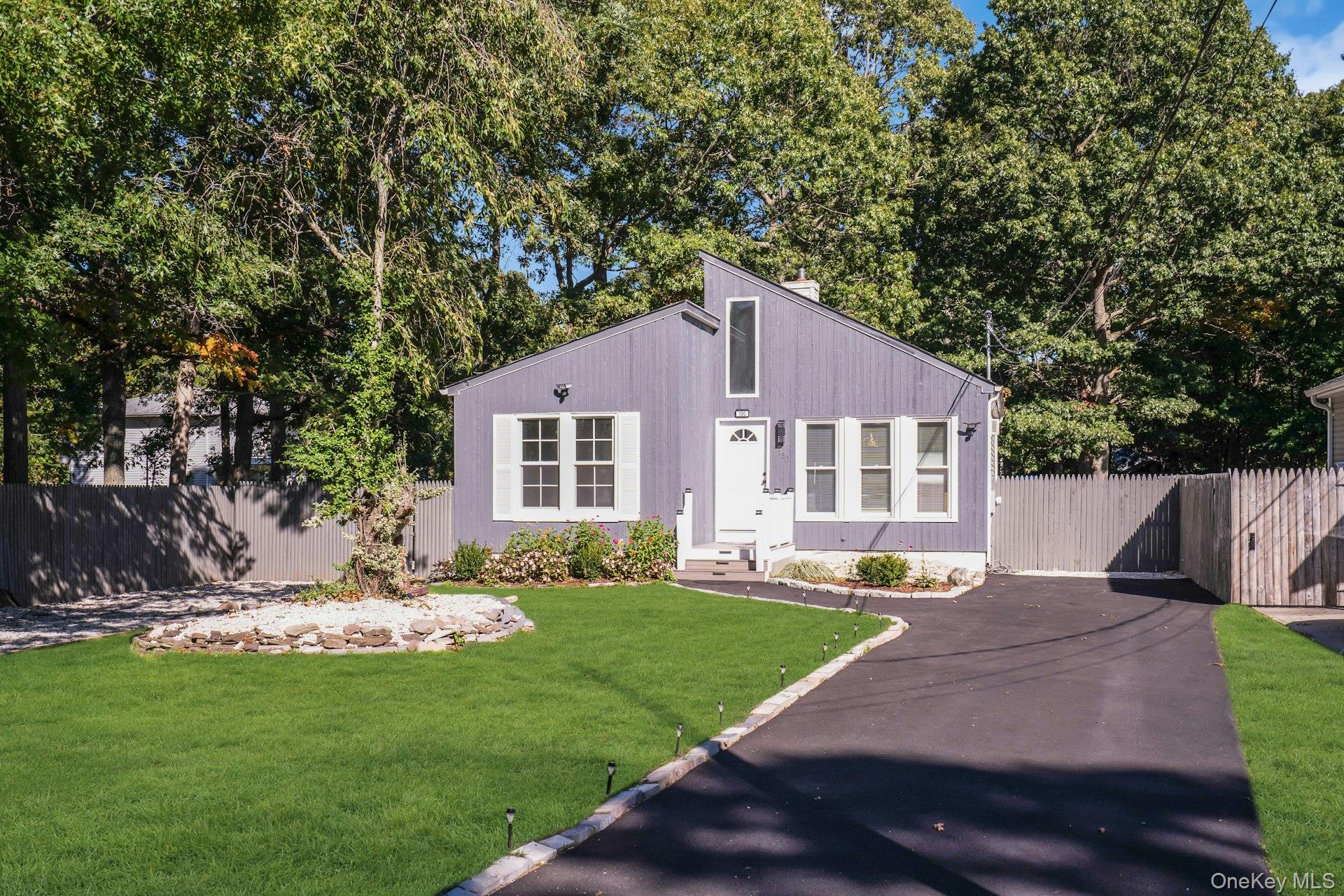 Gray-purple home with a tall angled roof, fenced yard, and landscaped lawn.