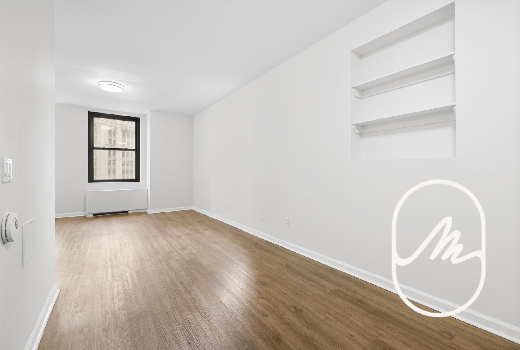 Empty room with light wood floors, built-in shelves, and a black-framed window.