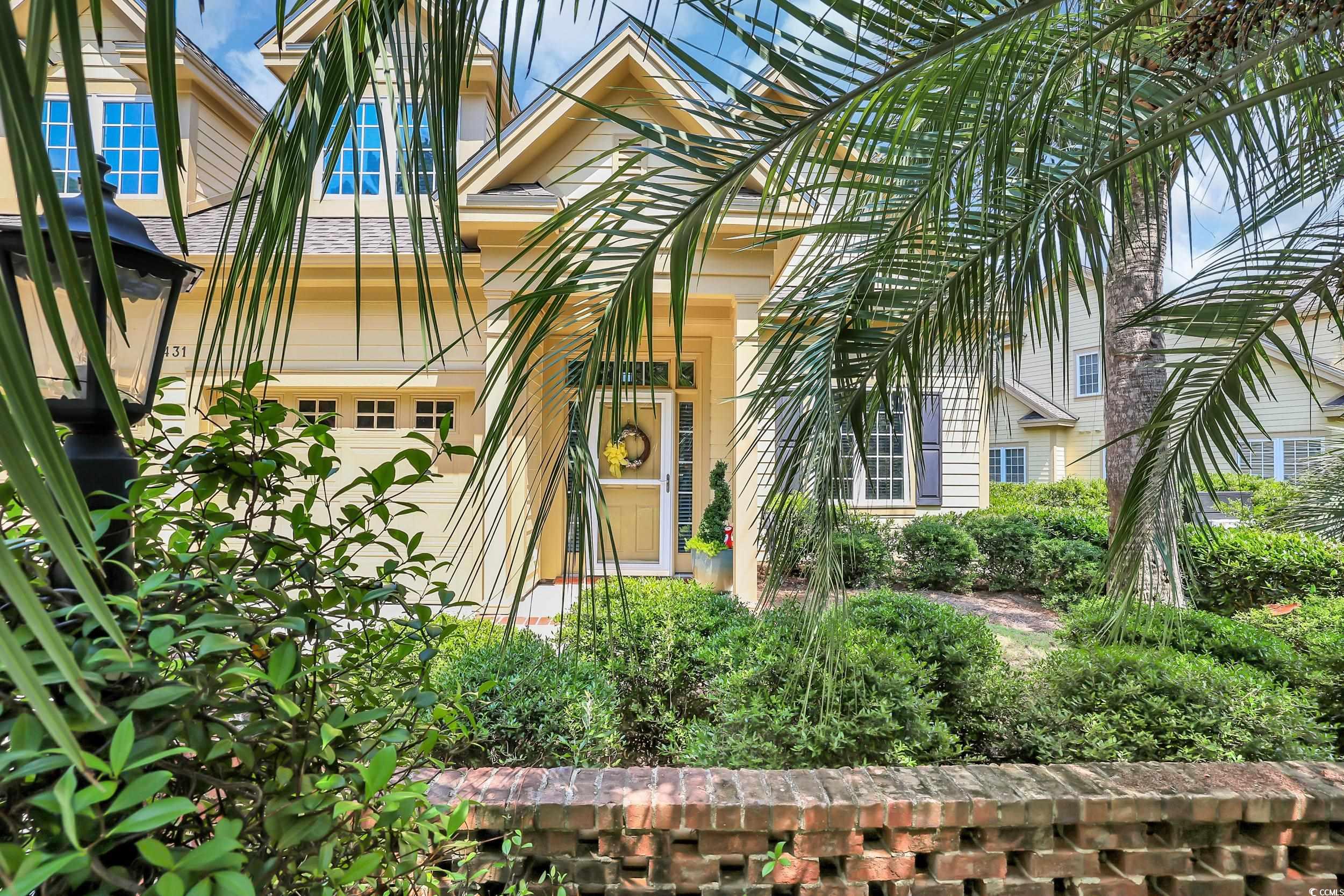 Harbor Club Villas home with a pale yellow entry, palm fronds, and landscaped garden.
