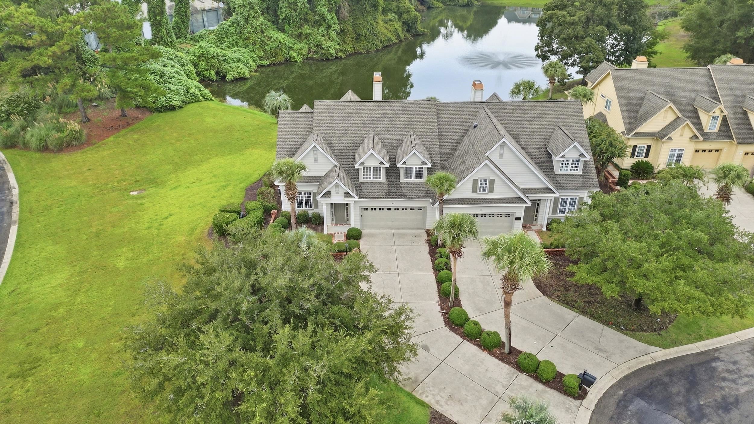 Gray villas with multiple garages beside a pond and landscaped lawn