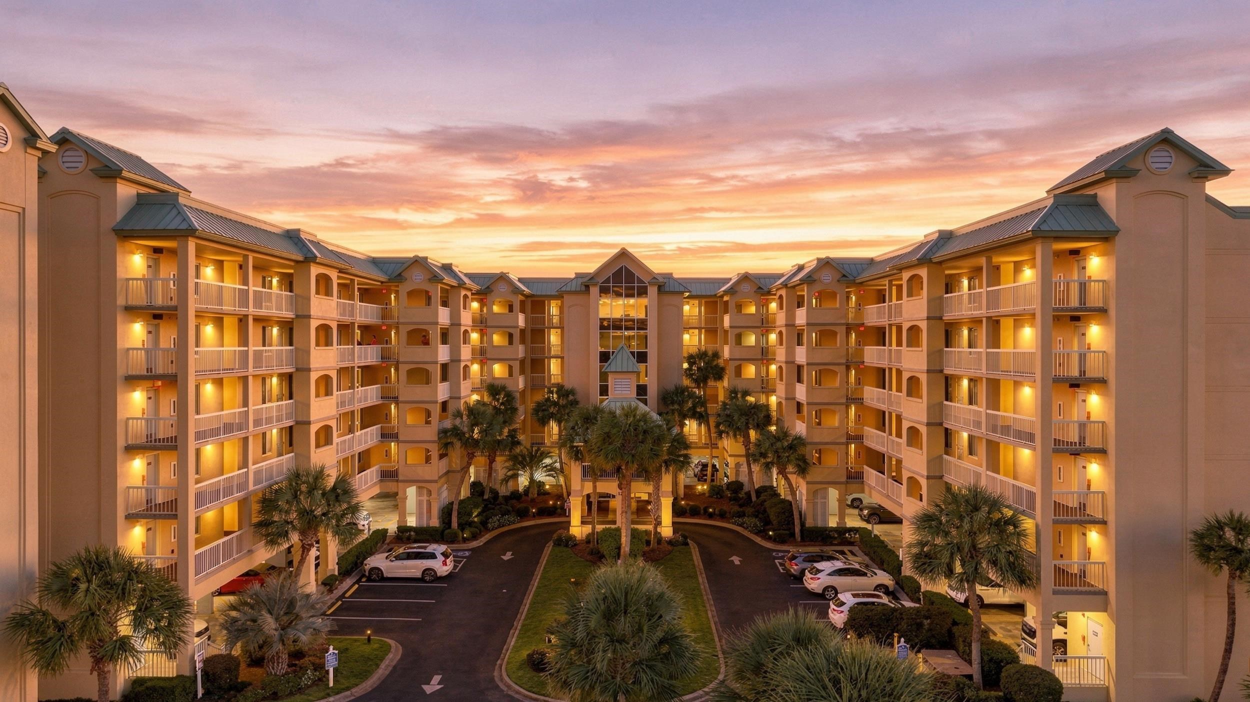 Condominium complex with a palm-lined courtyard and parking area at sunset.