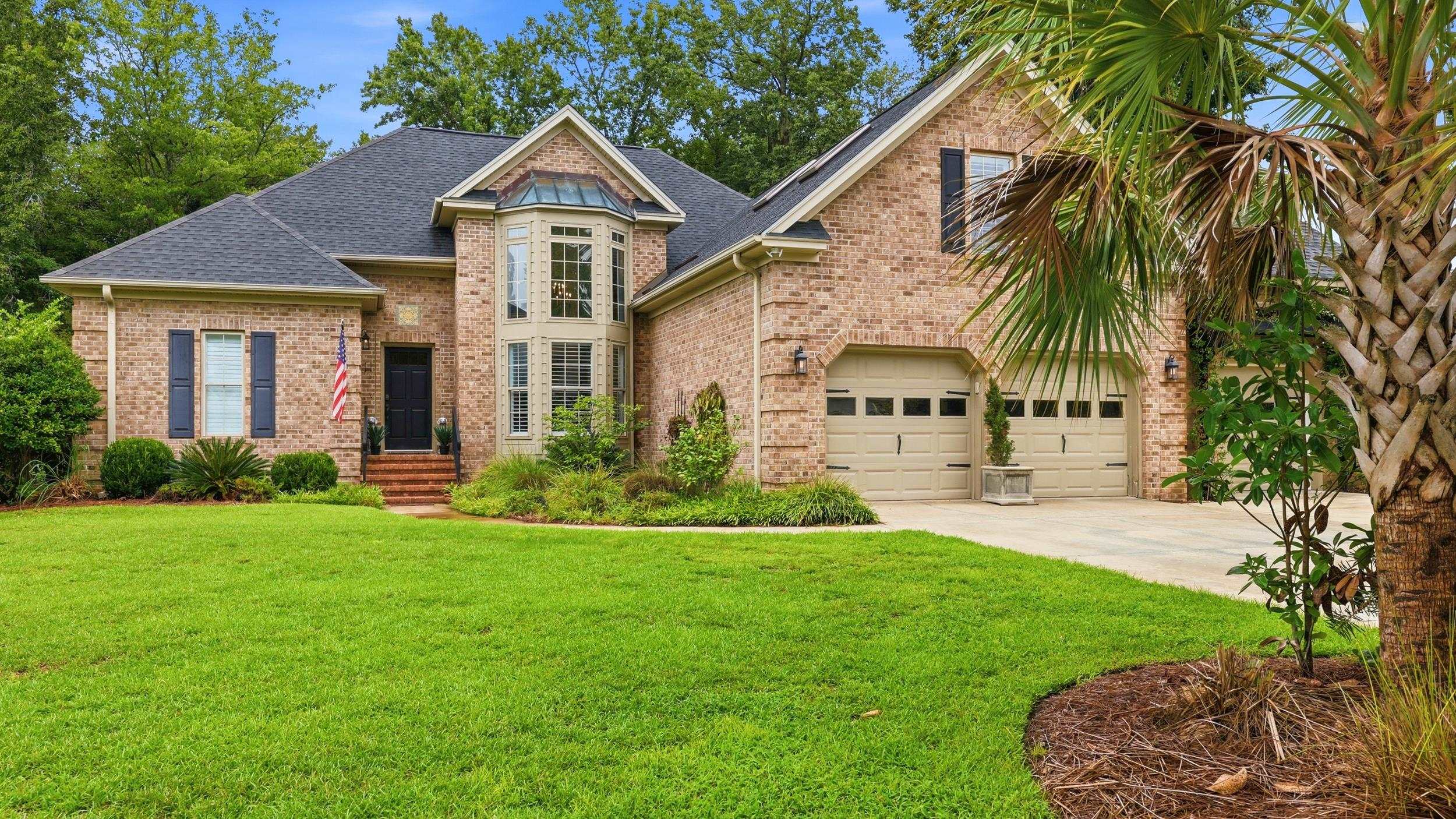 Brick house with a bay window, double garage, broad green lawn, and palm trees.