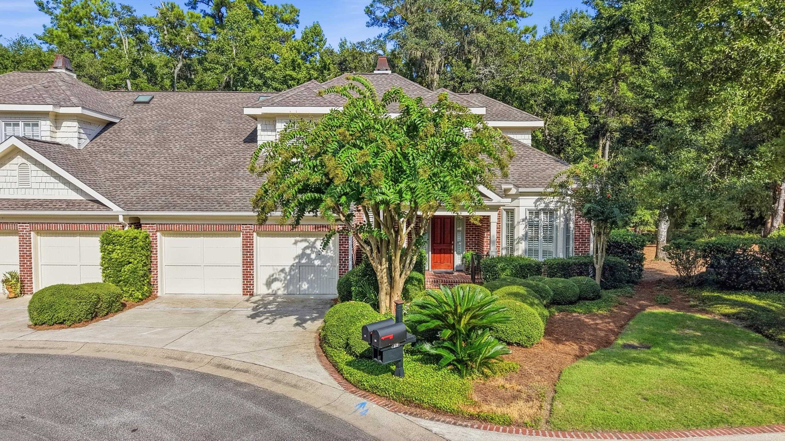 Brick-and-shingle villa with three garage doors, a red front door, and landscaped grounds.