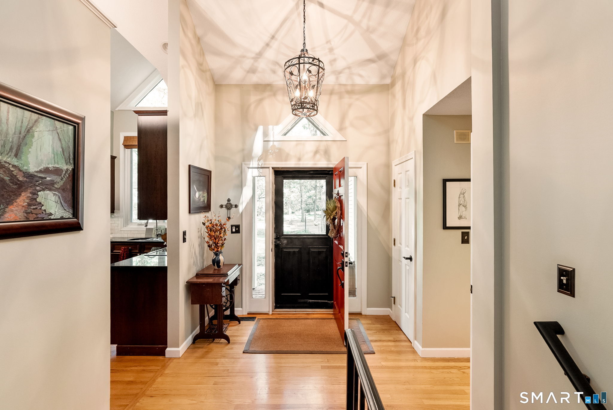 Foyer with vaulted ceiling, ornate lantern, hardwood floors, and an open red front door.