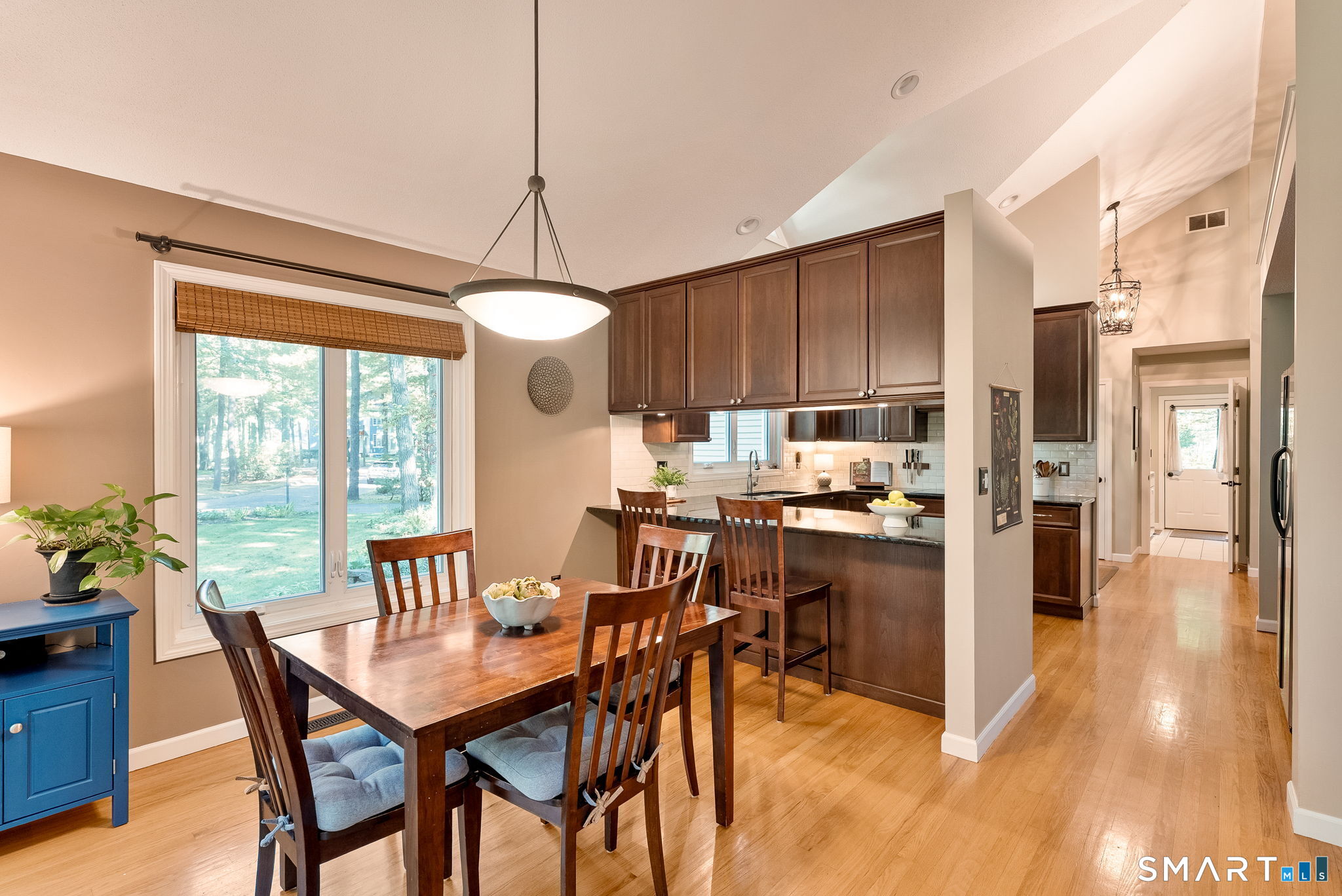 Dining area and kitchen with dark wood cabinetry, hardwood floors, and large windows overlooking trees.