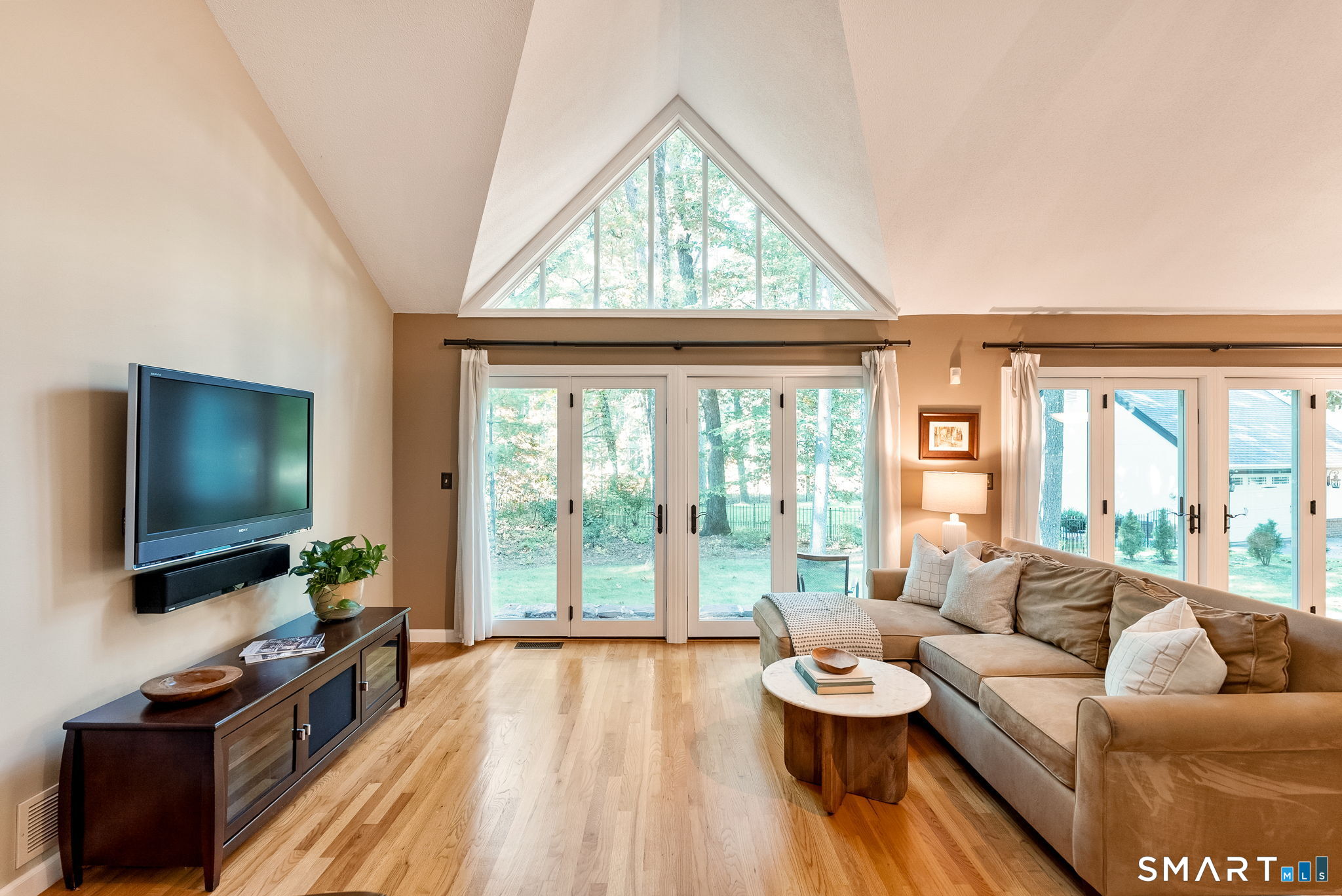Living room with vaulted ceiling, triangular window, French doors, hardwood floors, and sectional sofa.