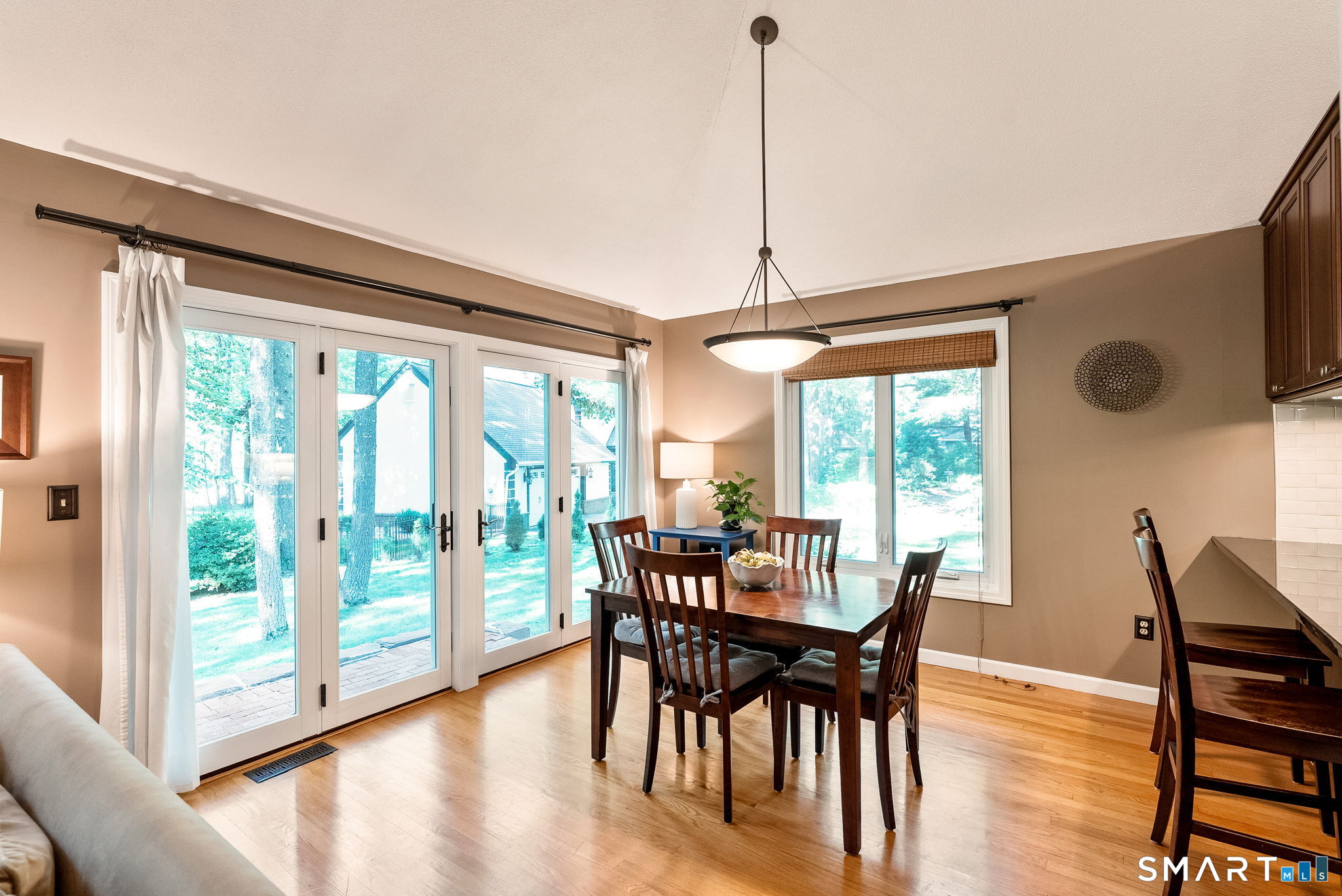 Dining area with a dark wood table, hardwood floors, and French doors overlooking trees.