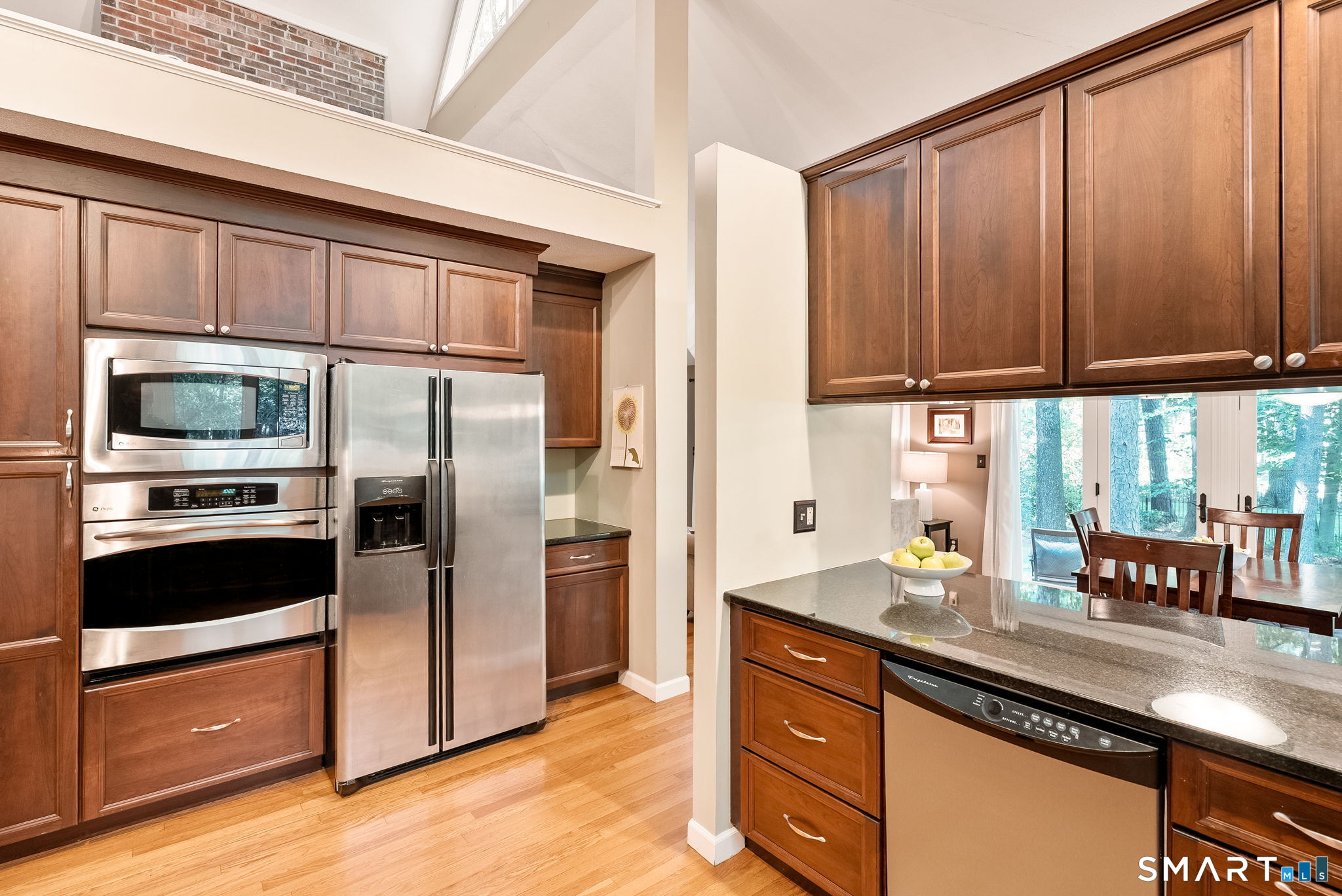 Kitchen with cherry cabinets, stainless-steel appliances, granite counters, and a peninsula overlooking a wooded dining area.