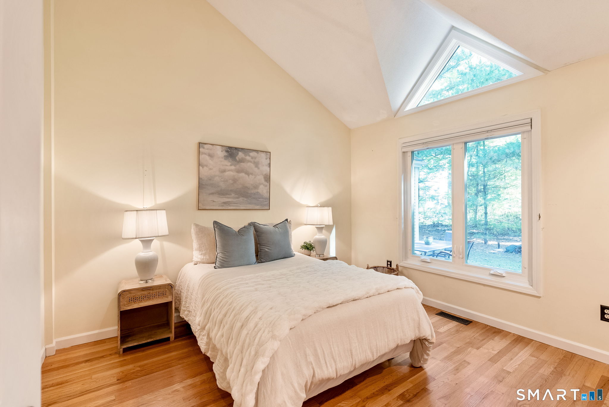 Staged bedroom with a white bed, wood floors, and a triangular skylight above the window.