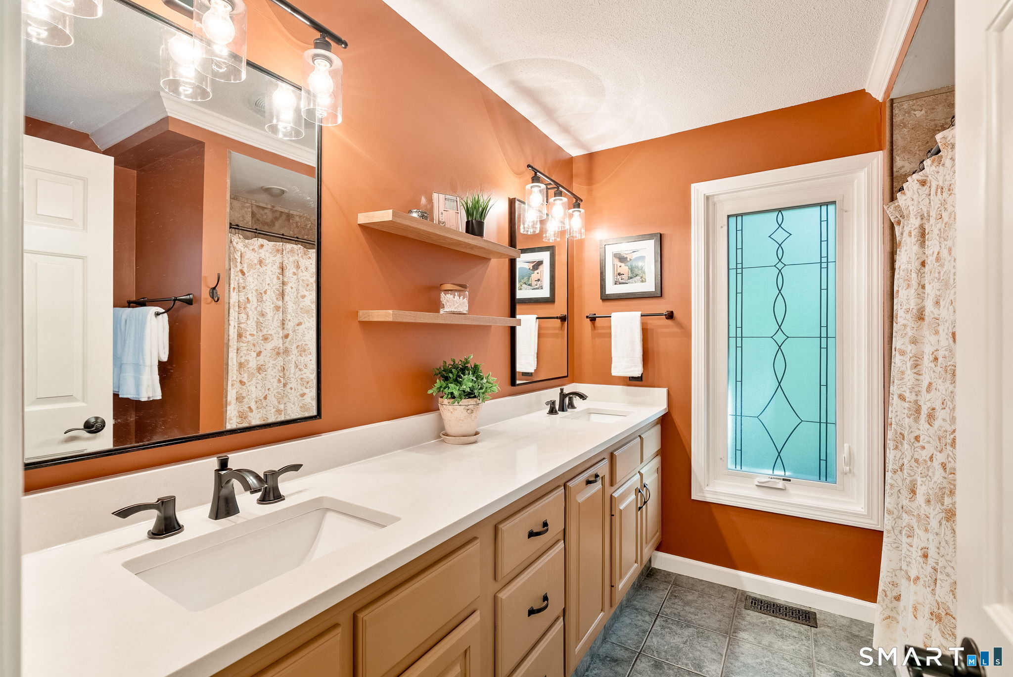 Bathroom with a double-sink vanity, terracotta walls, and a blue decorative glass window.