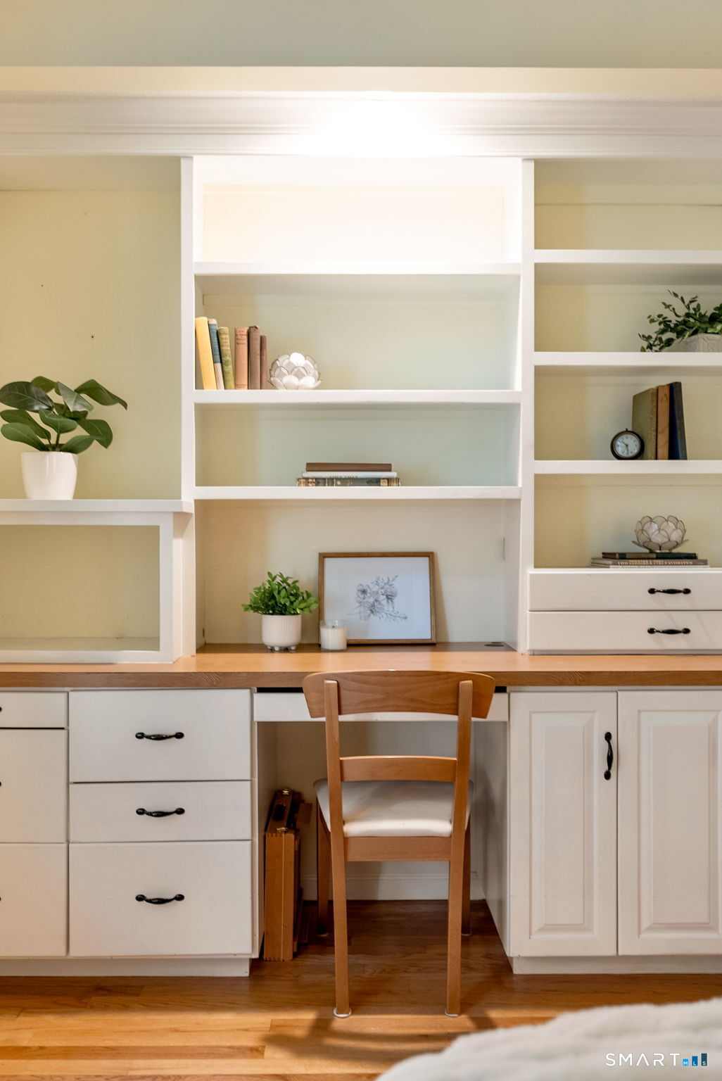 Built-in home office with white shelves, a wood desktop, and a wooden chair.